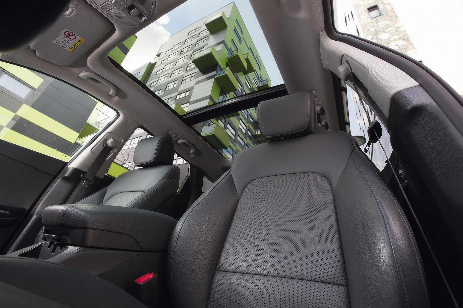Blick aus einem Auto mit offenem Glasdach auf moderne, grün-graue Gebäude.