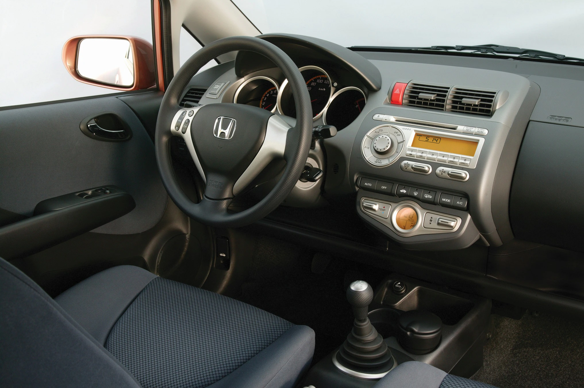 Innenraum eines Autos mit Honda-Logo am Lenkrad, Armaturenbrett mit Tacho, Radio, Klimasteuerung und manueller Gangschaltung.