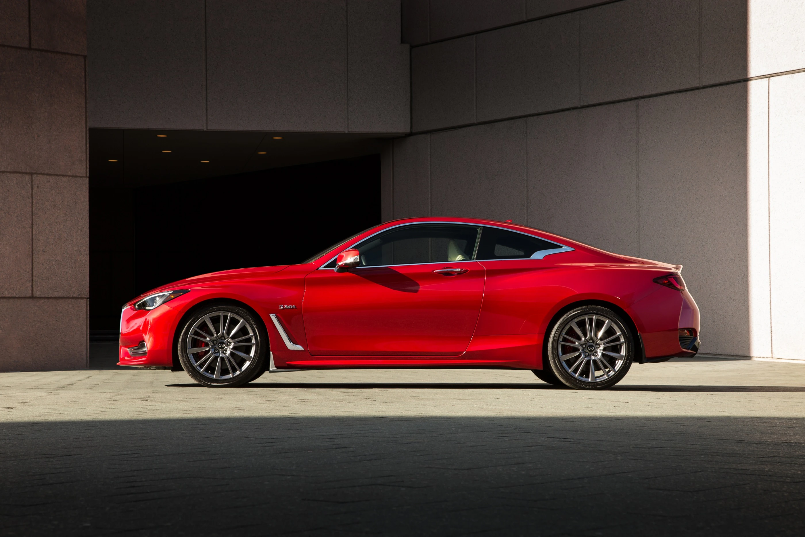 Rotes Sportcoupé parkend vor einem modernen Gebäude, seitliche Ansicht.