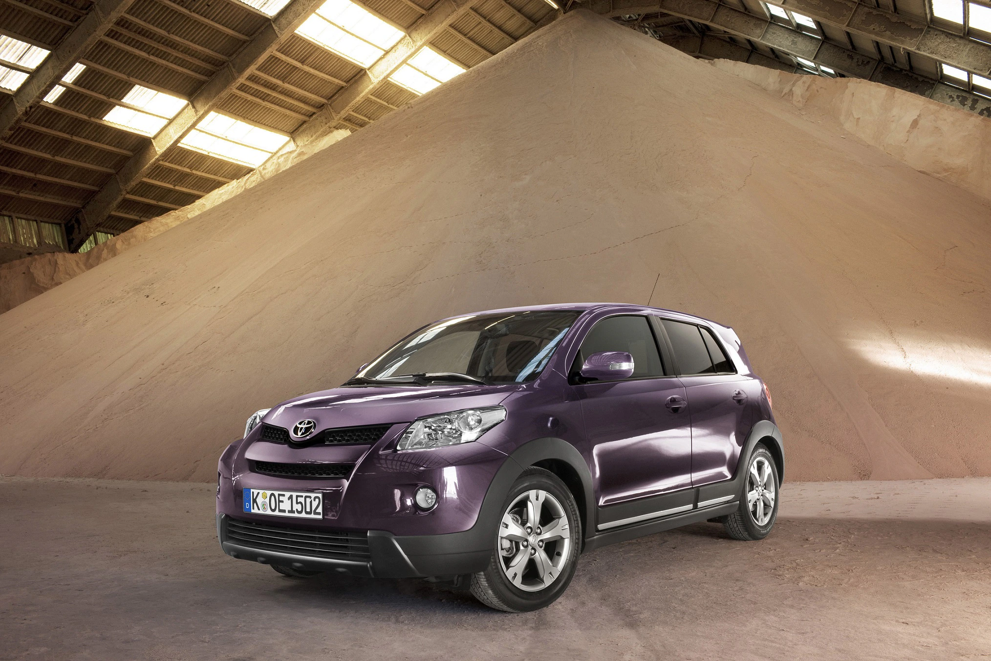 Lila SUV von Toyota steht in einem Lagerhaus vor einem großen Sandhaufen. Sonnenlicht fällt durch die Fenster auf das Auto.