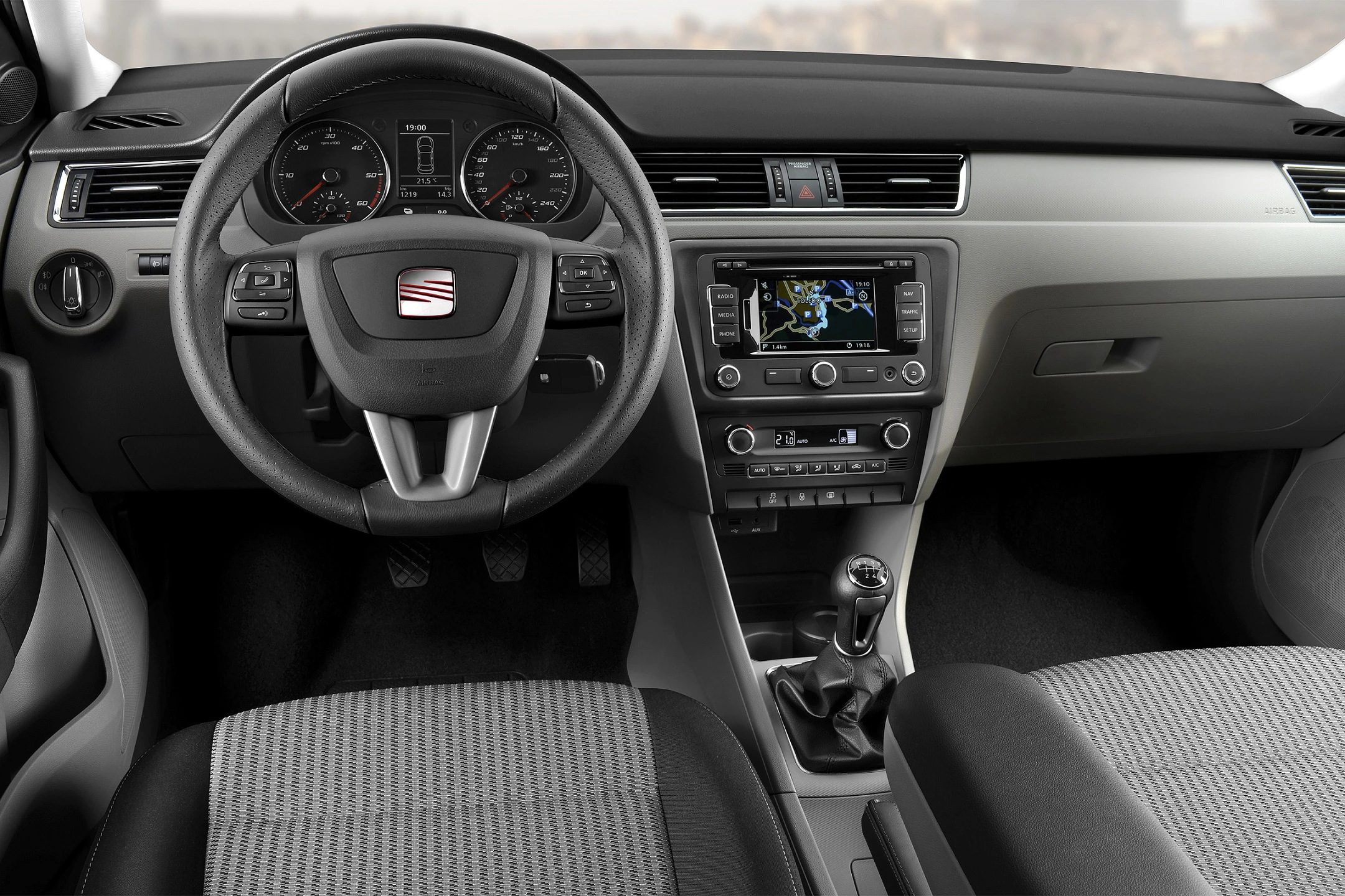 Innenraum eines Autos mit Lenkrad, Armaturenbrett, Tachometer und integriertem Navigationssystem. Stoffpolsterung auf den Sitzen.