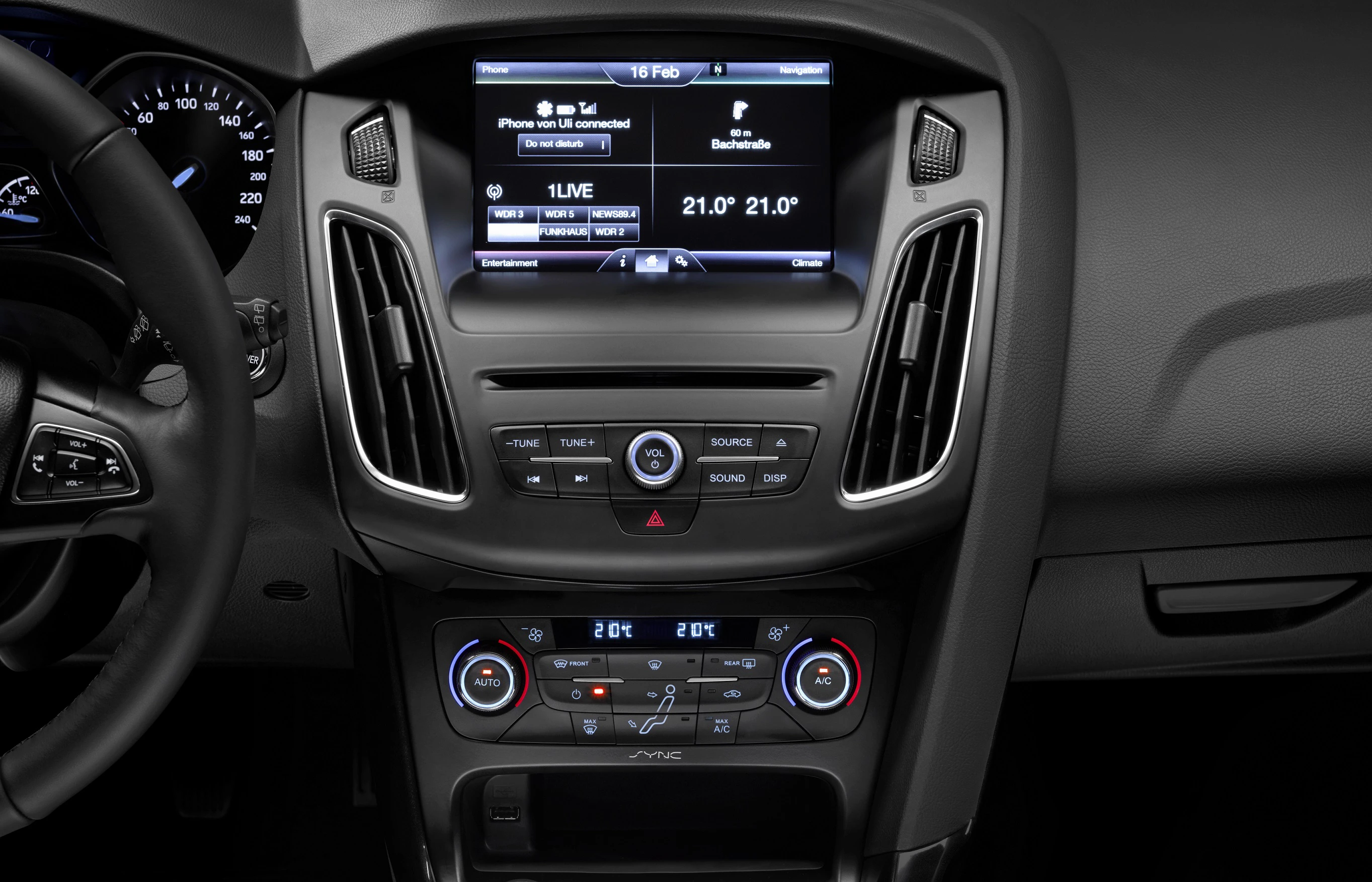 Nahaufnahme eines Fahrzeuginnenraums mit einem modernen Infotainment-System, Klimabedienung und Lüftungsschlitzen in der Mittelkonsole.