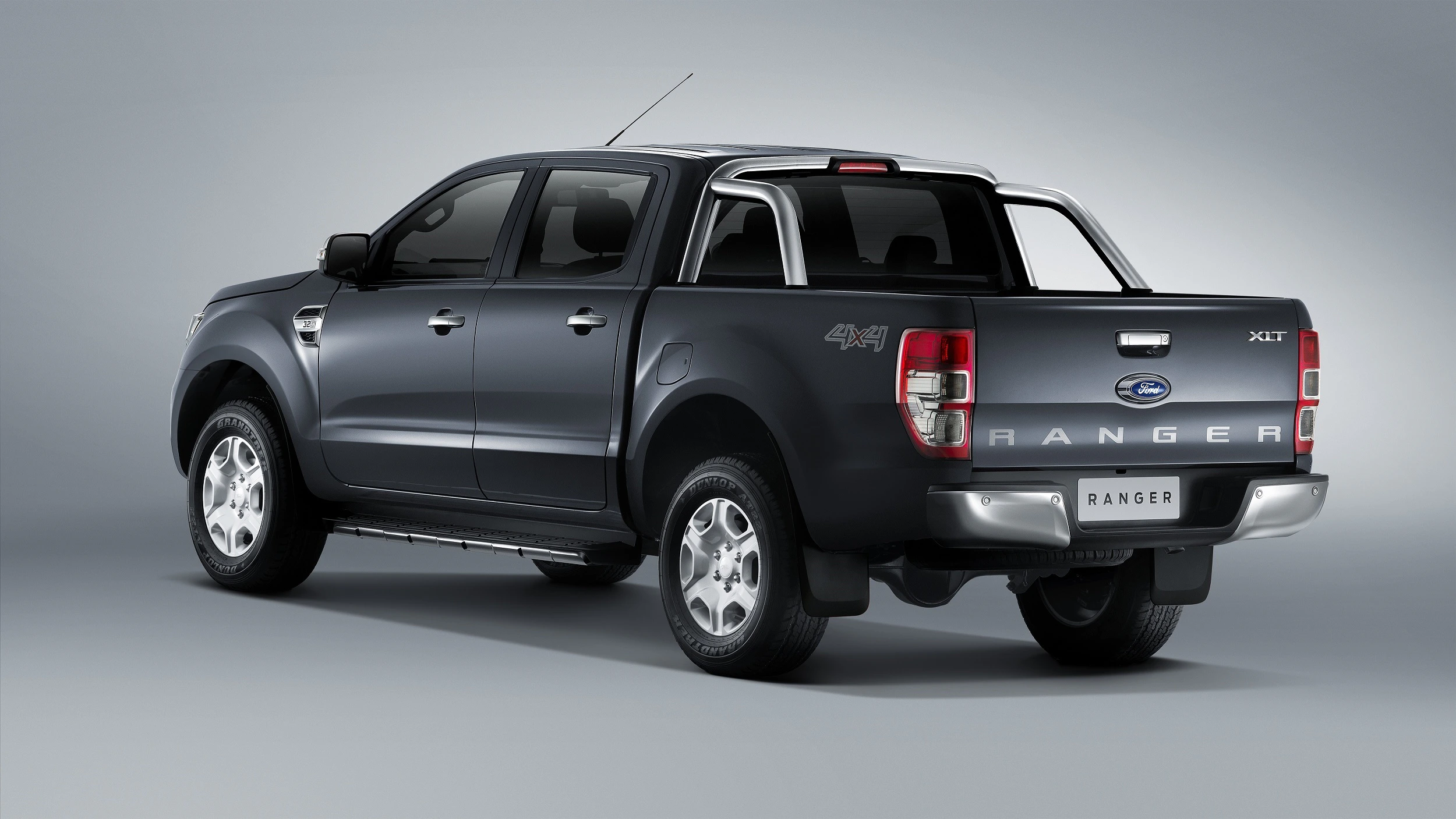 Ein grauer Ford Ranger XLT Pickup mit Doppelkabine, 4x4-Antrieb und Ladefläche, präsentiert sich in seitlicher Rückansicht vor grauem Hintergrund.
