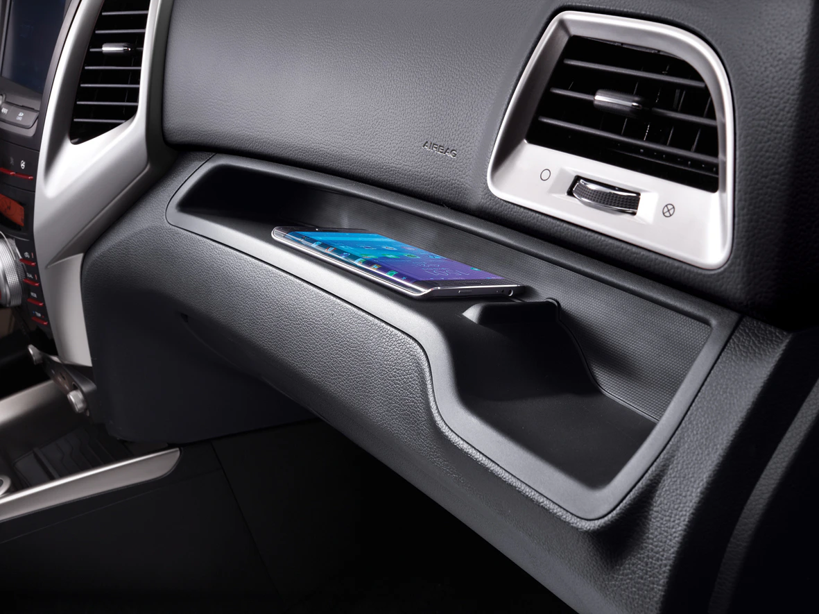 Smartphone auf einer Ablage im Autoinnenraum neben Lüftungsschlitzen und Armaturenbrett aus schwarzem Leder.
