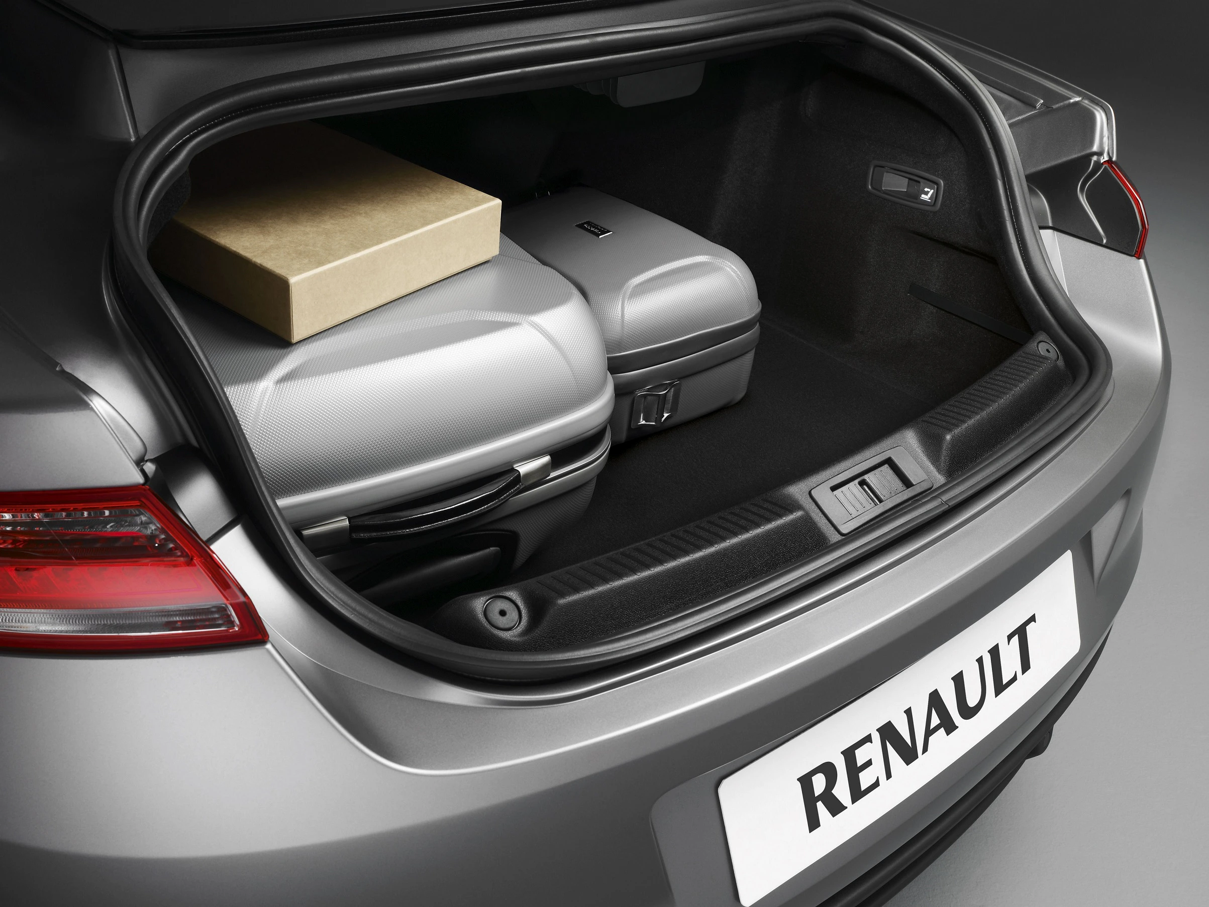 Offener Kofferraum eines Renaults mit einem grauen Koffer und einem braunen Karton auf dunkelgrauem Teppichboden.