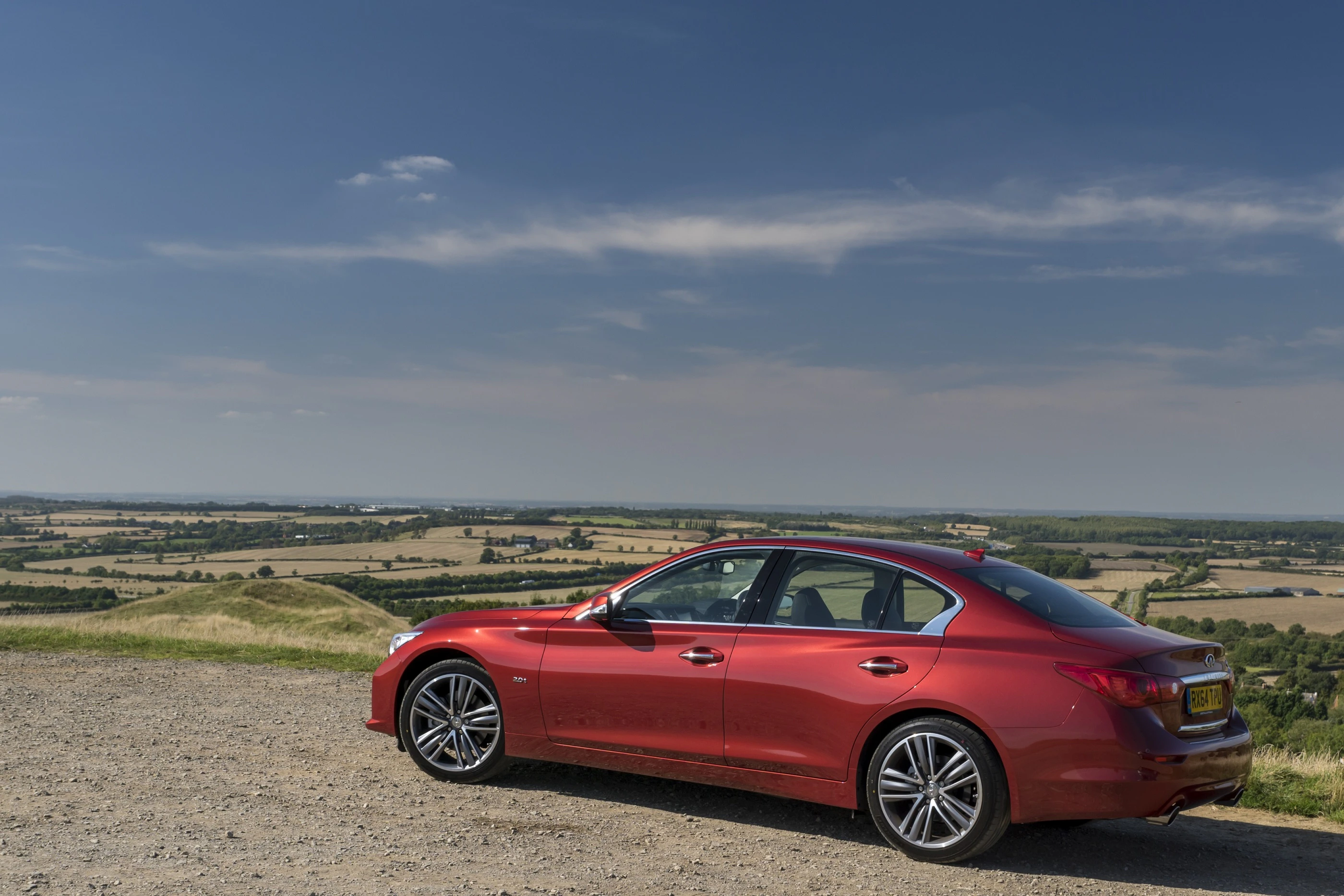 Roter Sportwagen parkt auf einem Hügel mit weitem Blick über eine flache, bewirtschaftete Landschaft unter klarem, blauem Himmel.