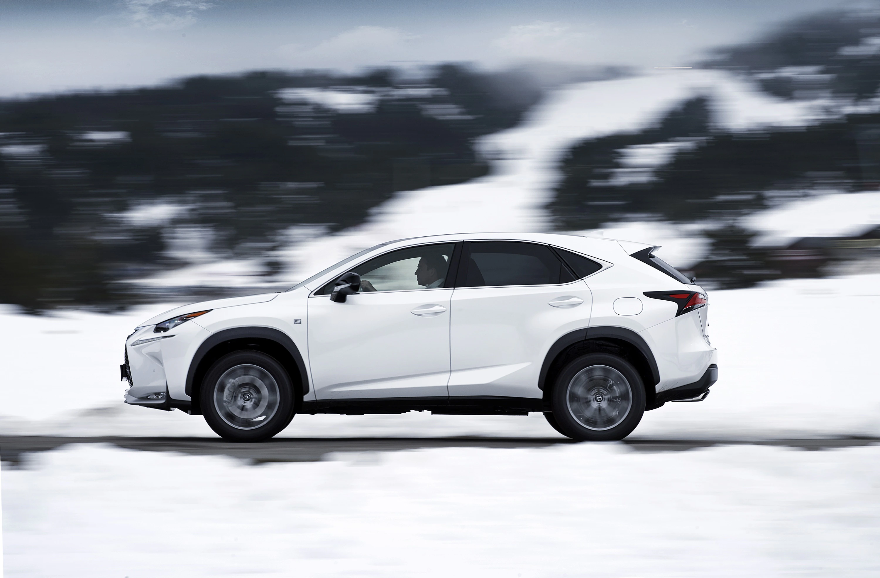 Weißer SUV fährt durch schneebedeckte Landschaft mit bewaldeten Hügeln im Hintergrund.