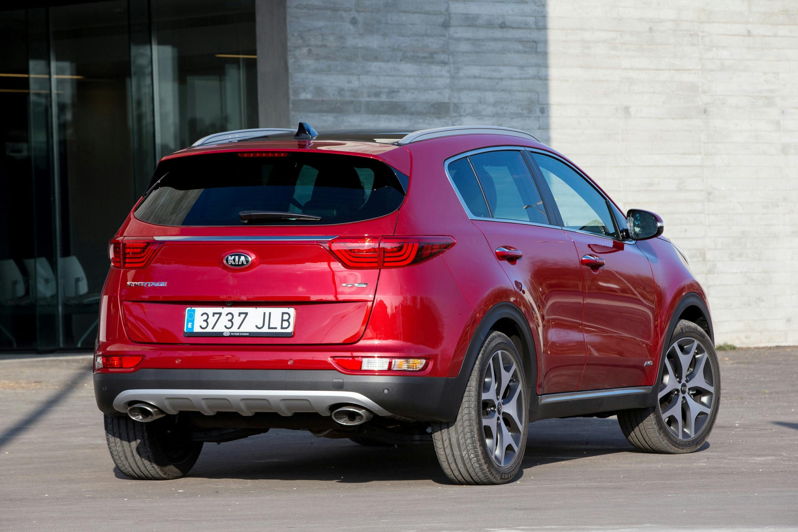 Roter Kia-SUV, Modell Sportage, geparkt vor einem modernen Gebäude. Rückansicht mit spanischem Kennzeichen.