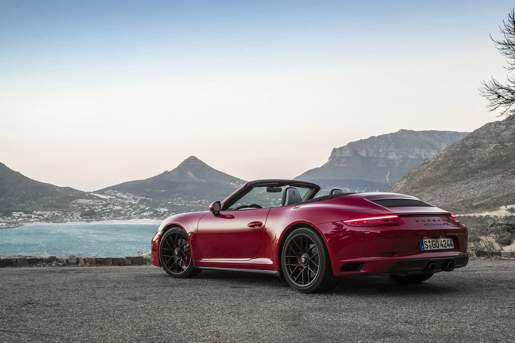 Roter Sportwagen auf Küstenstraße, Meer und Berge im Hintergrund, klarer Himmel. Cabrio mit sportlichem Design.