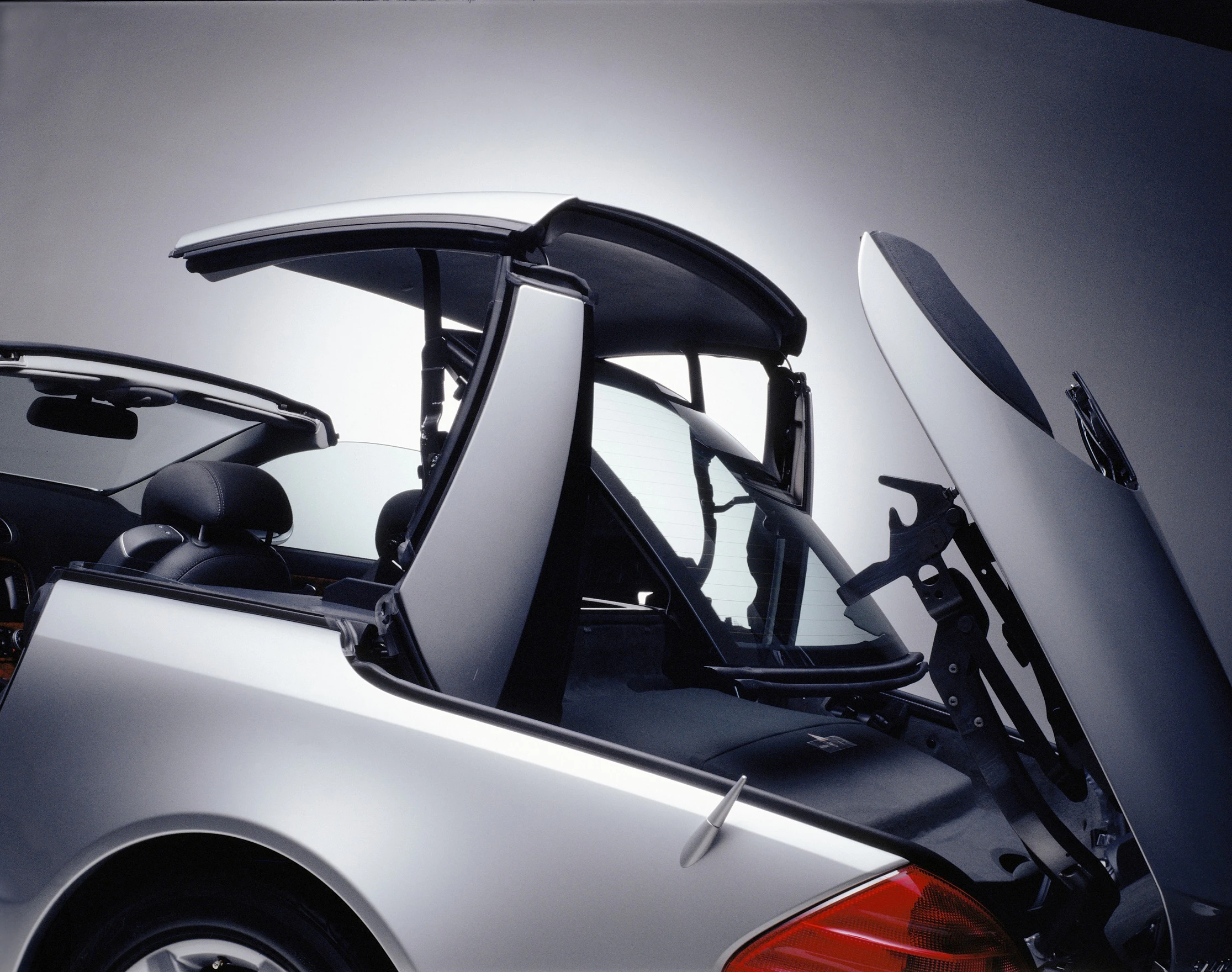 Silbernes Cabrio mit ausfahrbarem Hardtop, im Prozess des Umwandelns vom Cabrio zum Coupé, vor neutralem Hintergrund.