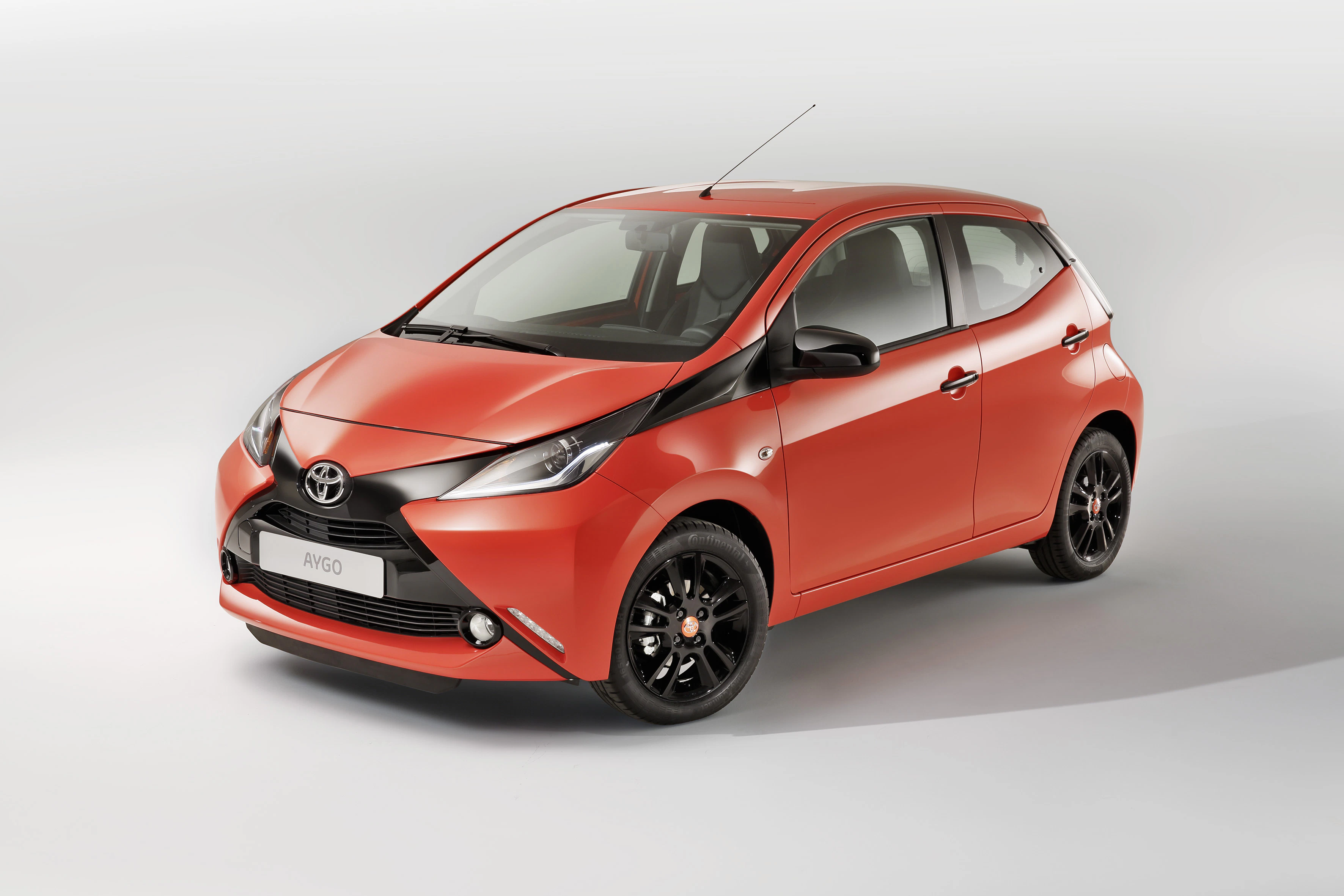 Kompakter, roter Toyota Aygo mit modernen Scheinwerfern und schwarzen Rädern, auf hellgrauem Hintergrund abgebildet.