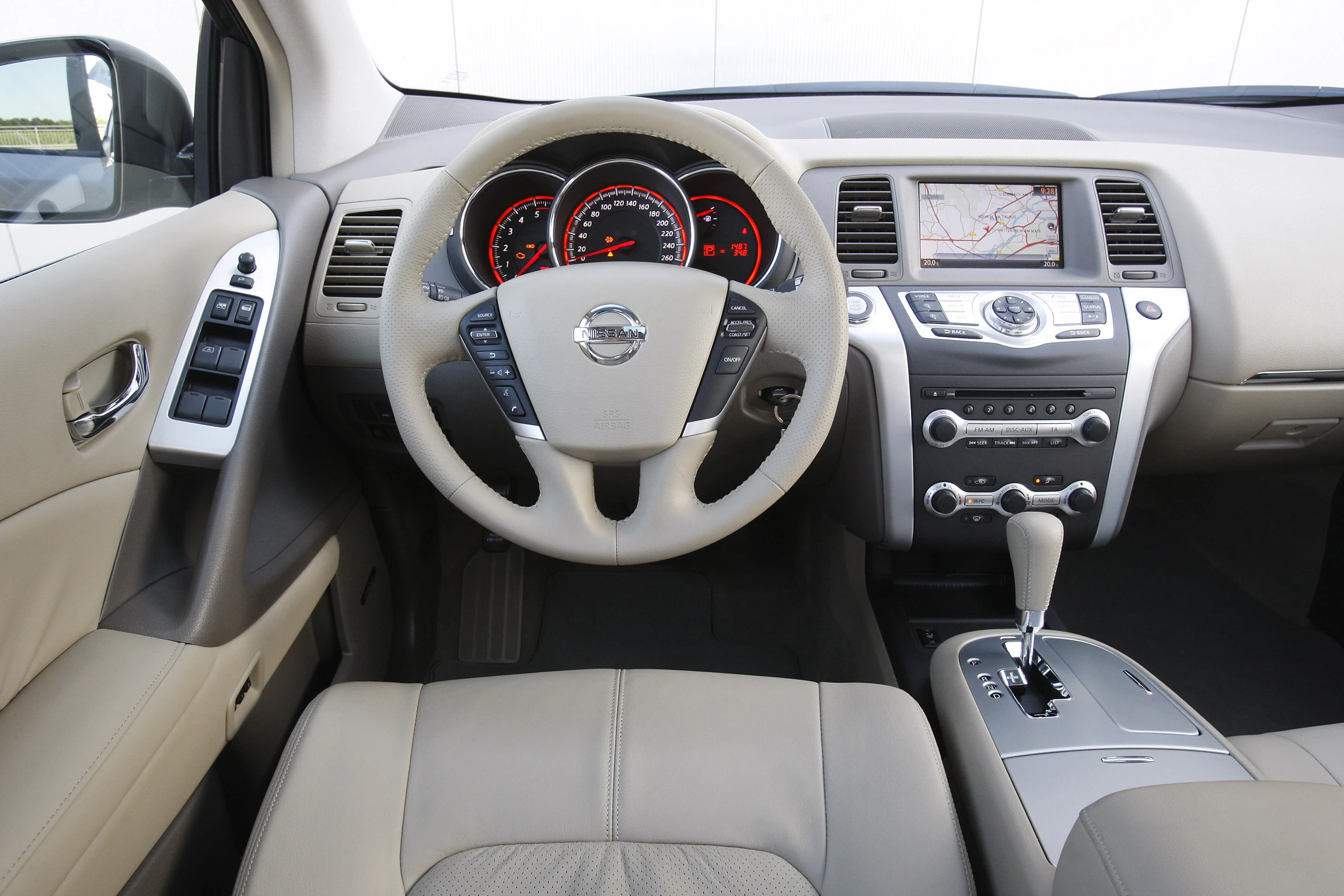 Innenraum eines Autos mit beigem Lederlenkrad, Tachometern, Navigationssystem und Automatikwählhebel in der Mittelkonsole.