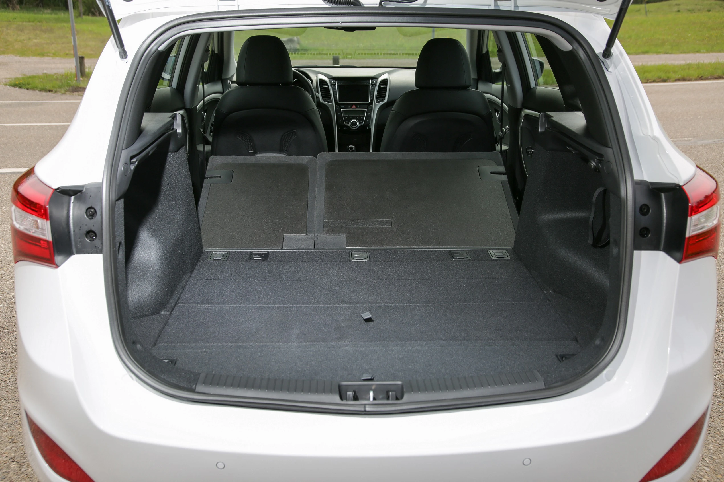 Rückansicht eines geöffneten Kofferraums eines weißen Autos mit umgeklappten Rücksitzen. Die Ladekapazität ist vergrößert.