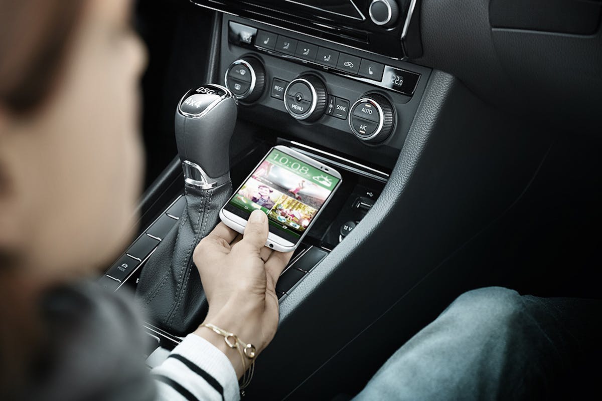 Eine Person im Auto hält ein Smartphone mit einem Spiel auf dem Bildschirm. Das Handy liegt in der Mittelkonsole neben dem Schalthebel.