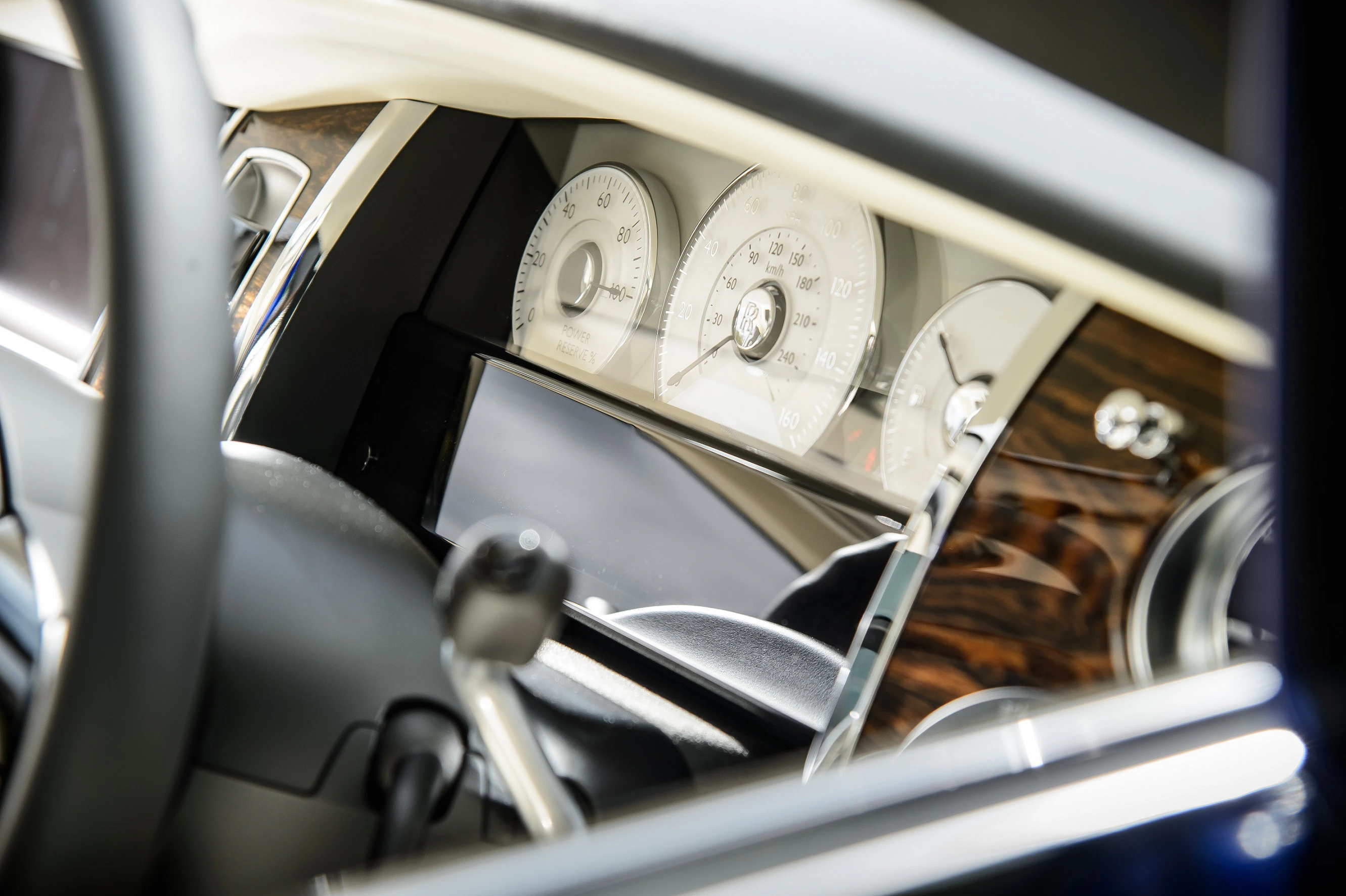 Nahaufnahme eines Autoinnenraums mit Fokus auf das Armaturenbrett, darunter ein Tachometer und Holzverkleidung.