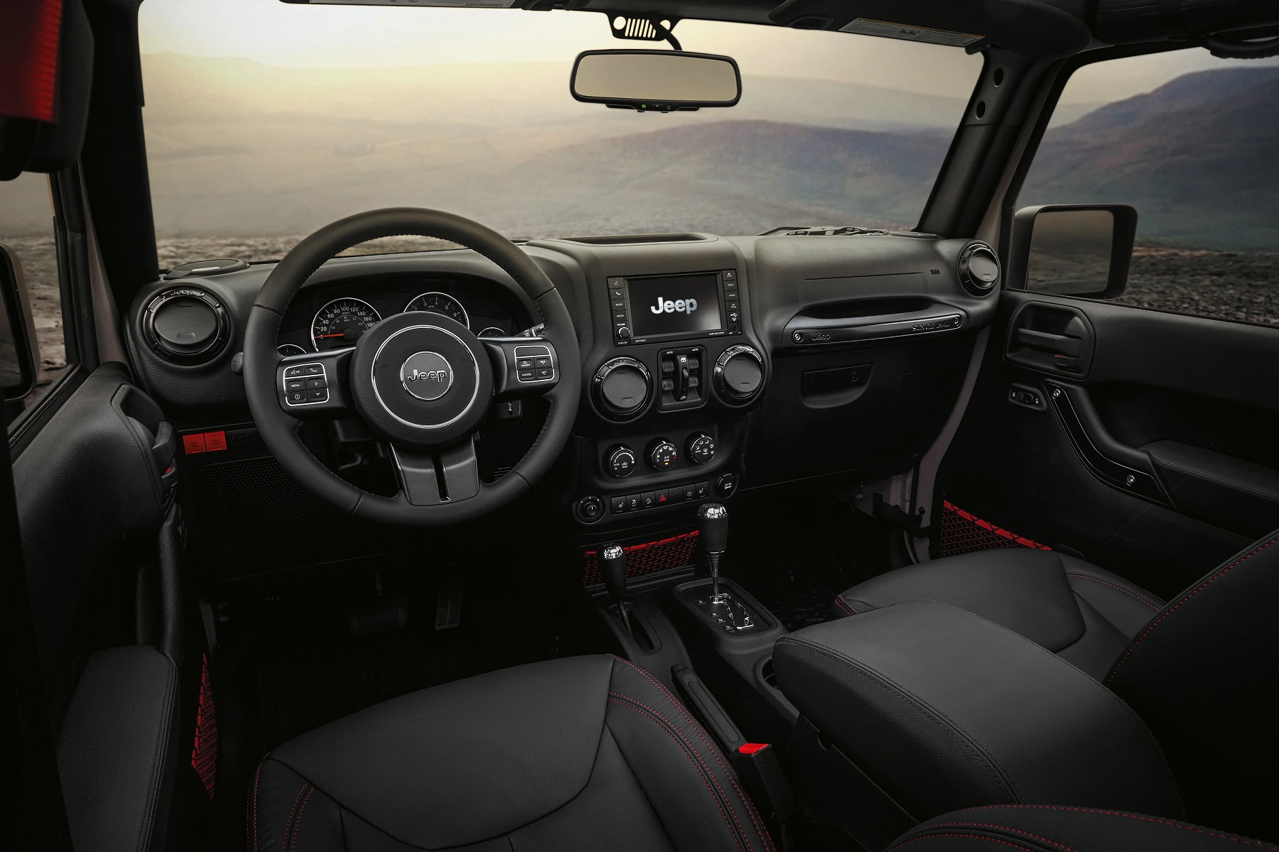 Innenraum eines Jeep mit schwarzem Leder, Lenkrad mit Markenlogo, Touchscreen und Blick auf eine bergige Landschaft durch die Frontscheibe.