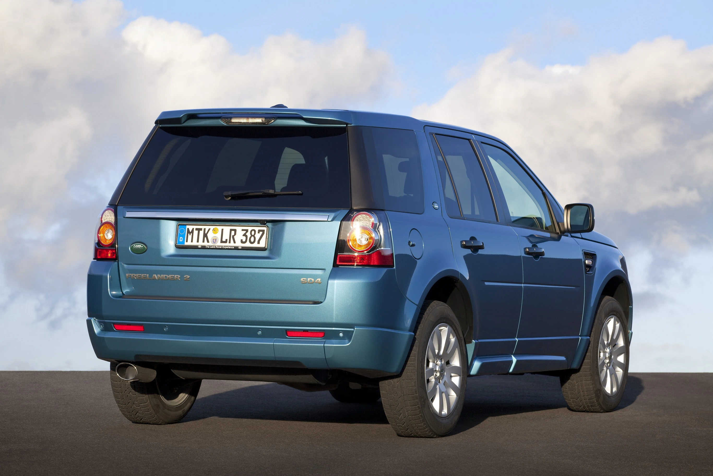 Blauer SUV auf einer Straße, gesehen von hinten, mit deutscher Nummerntafel und bewölktem Himmel im Hintergrund.