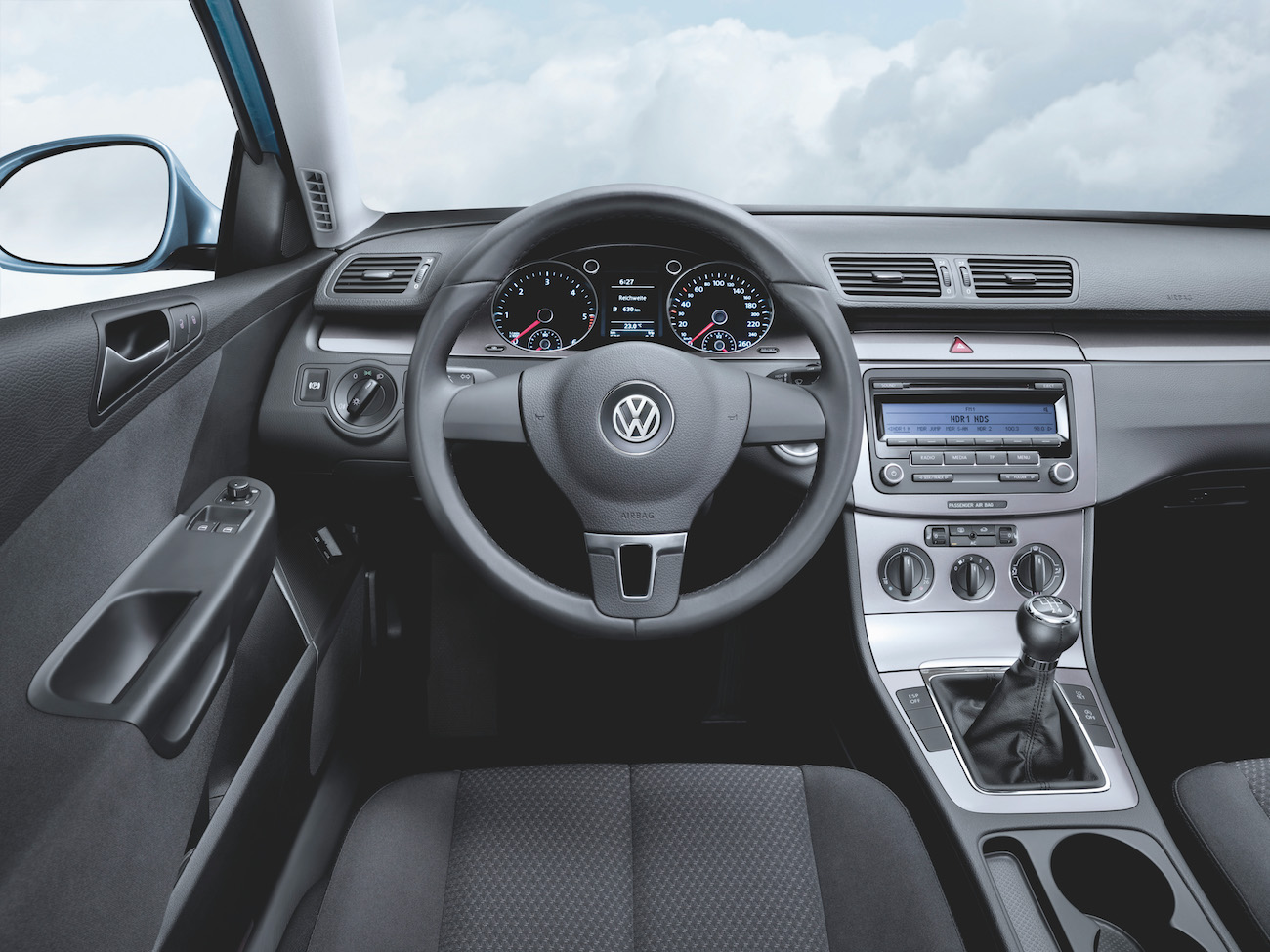 Volkswagen-Autoarmaturenbrett mit Lenkrad, Tachometer, und Schalthebel. Graues Interieur mit schwarzen Akzenten und Radioanzeige.