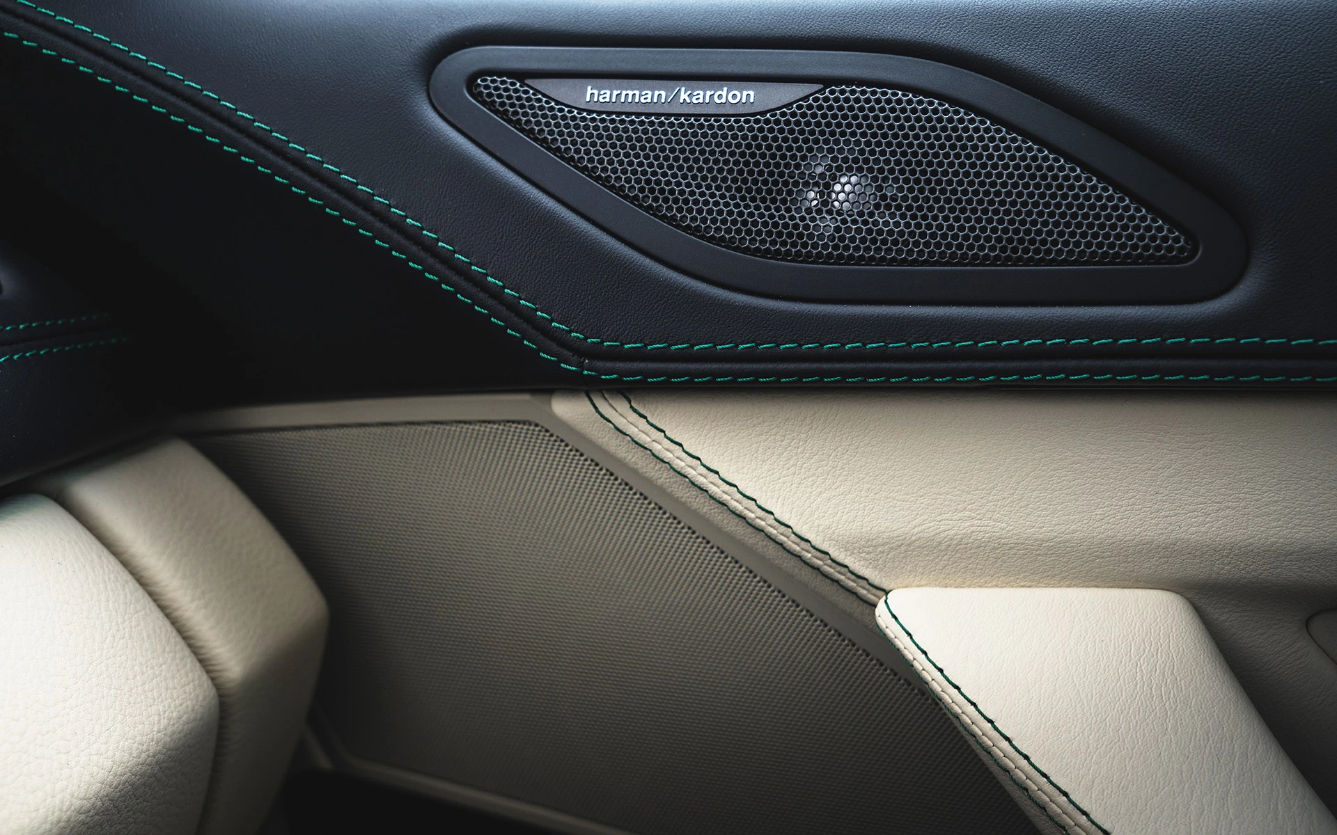 Nahaufnahme eines Autoinnenraums mit einem schwarzen harman/kardon Lautsprecher und beigen Ledersitzen, betont durch grüne Nähte.