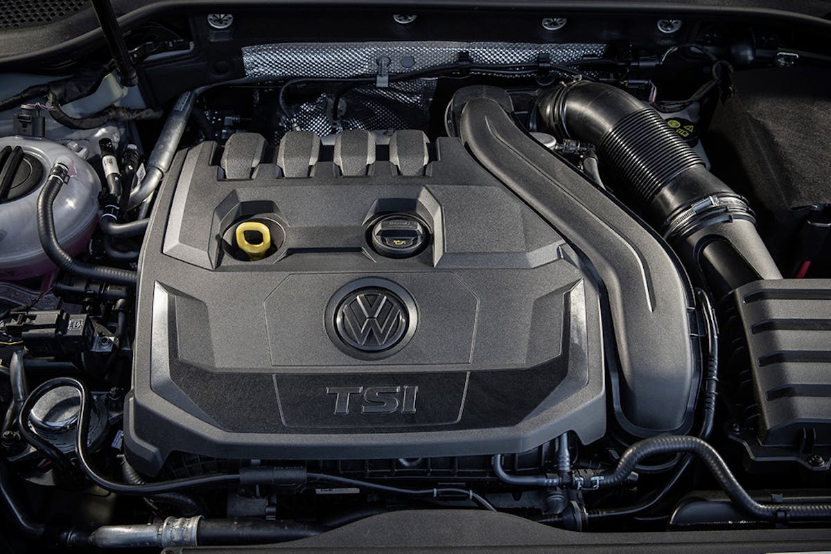 Motorraum mit einem TSI-Motor von Volkswagen, detailreiche Ansicht mit sichtbarem VW-Logo auf der Motorabdeckung, umgeben von Schläuchen und Teilen.
