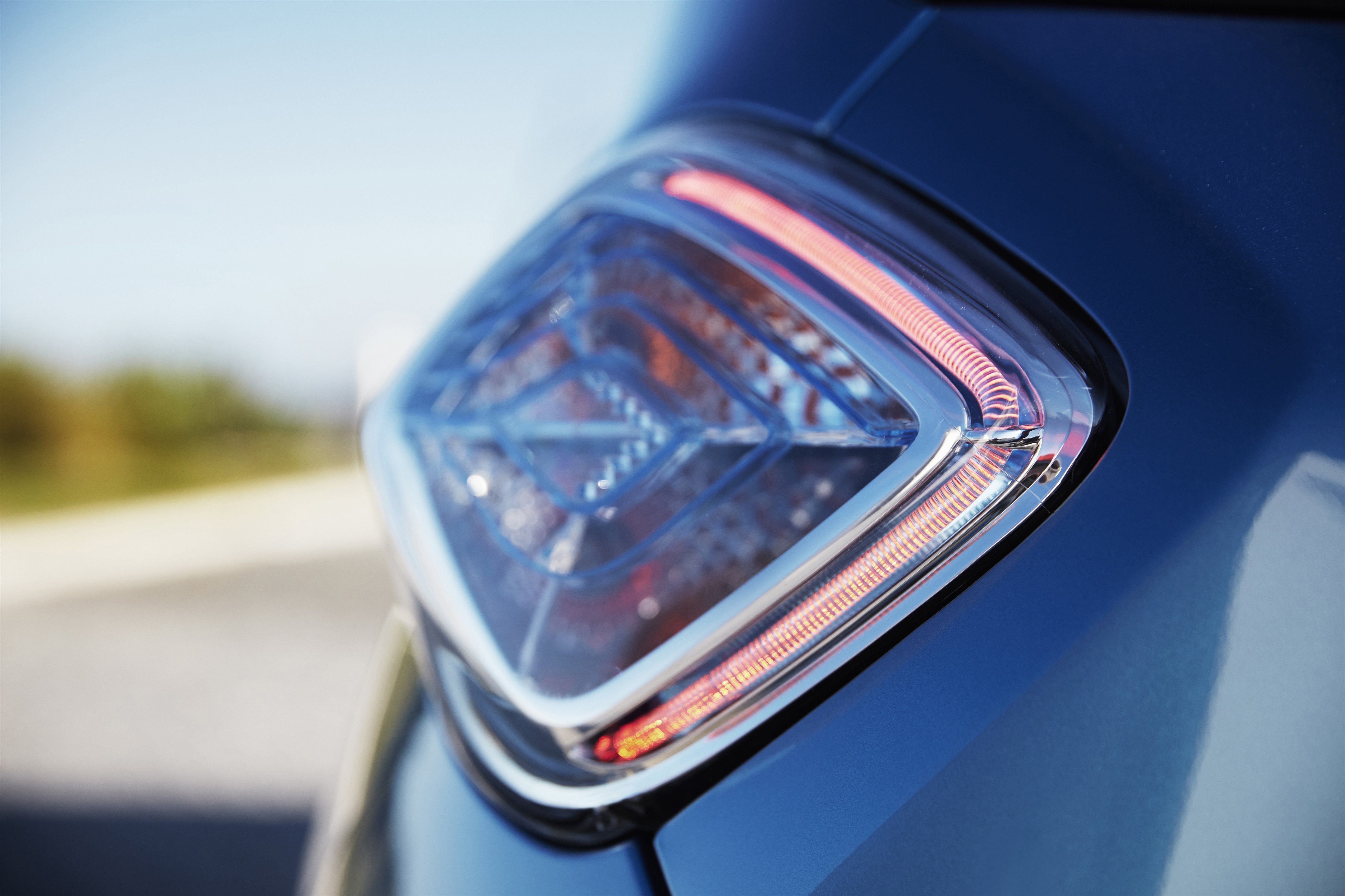 Nahaufnahme eines modernen, blauen Fahrzeugs mit eingeschaltetem Rücklicht, das am Rand einer Straße geparkt ist.