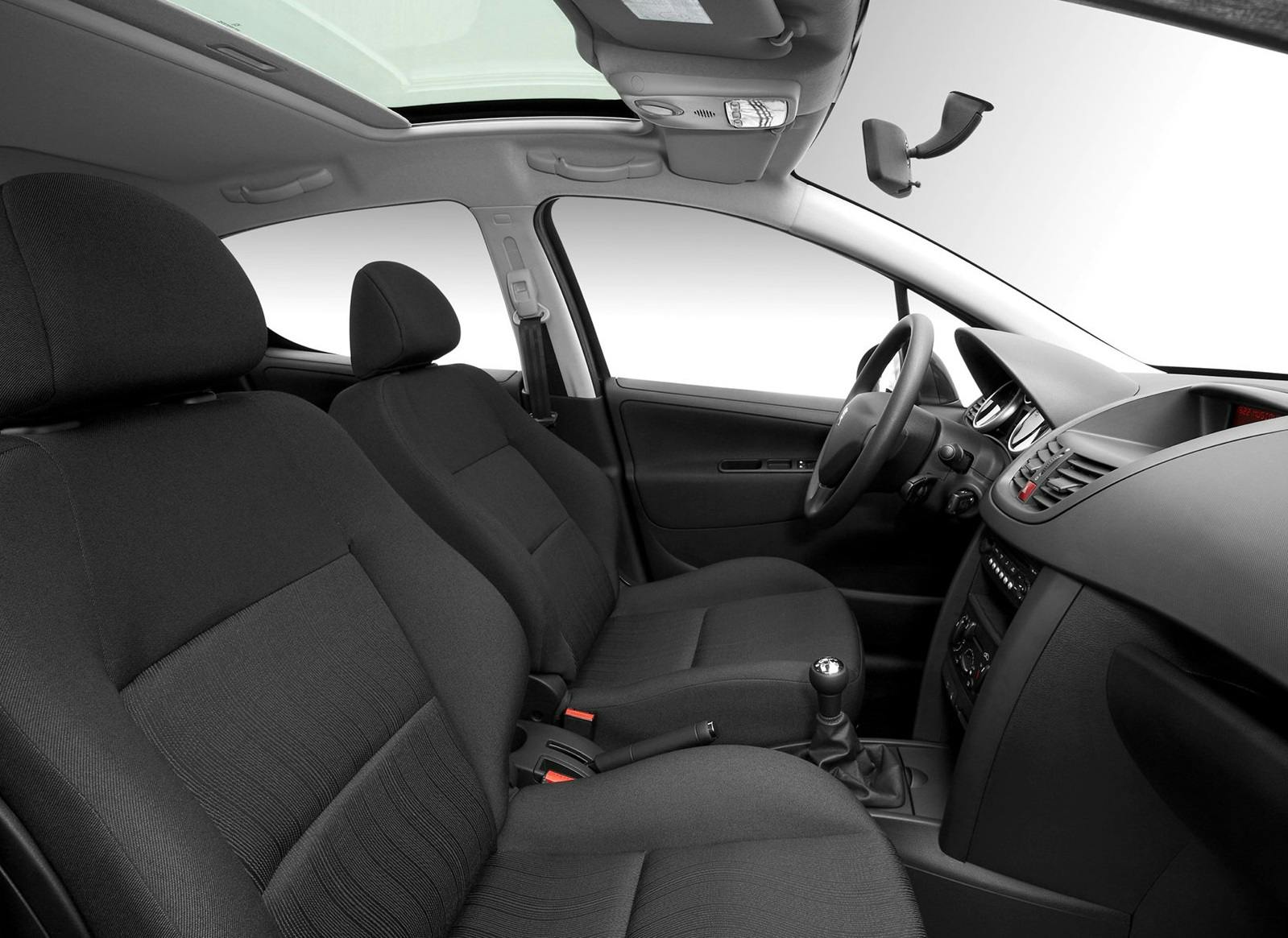 Autoinnenraum mit zwei schwarzen Vordersitzen, Schalthebel, Armaturenbrett und Lenkrad. Helles Licht kommt durch das Glasdach.