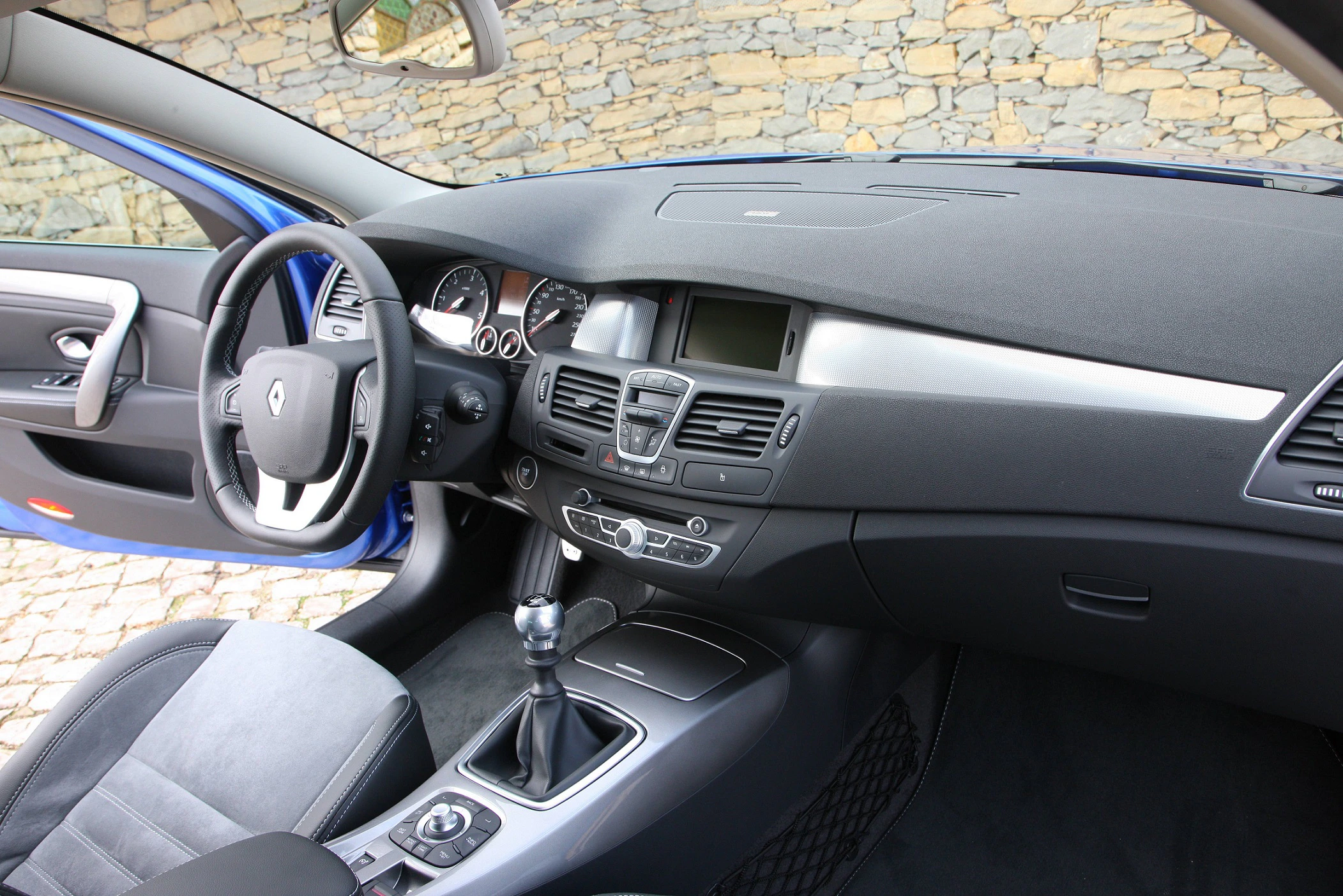 Innenraum eines Autos mit grauer, moderner Ausstattung, sichtbarem Lenkrad, Schalthebel und einem Armaturenbrett mit mehreren Anzeigen.