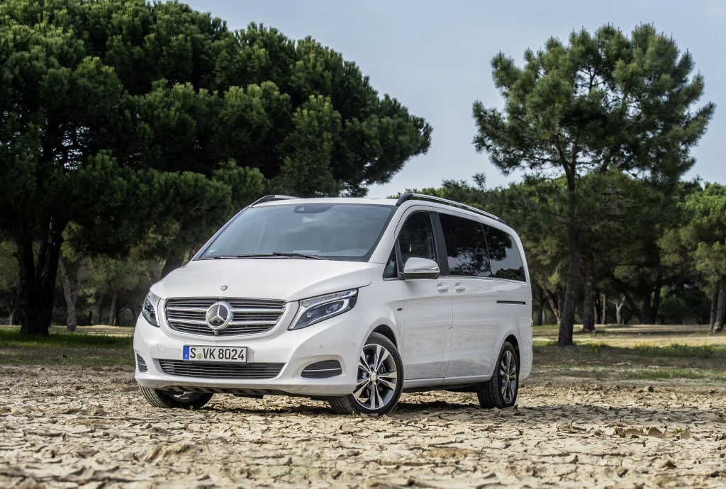 Ein weißer Mercedes-Benz Van geparkt auf einem trockenen, sandigen Gelände mit Kiefern im Hintergrund.