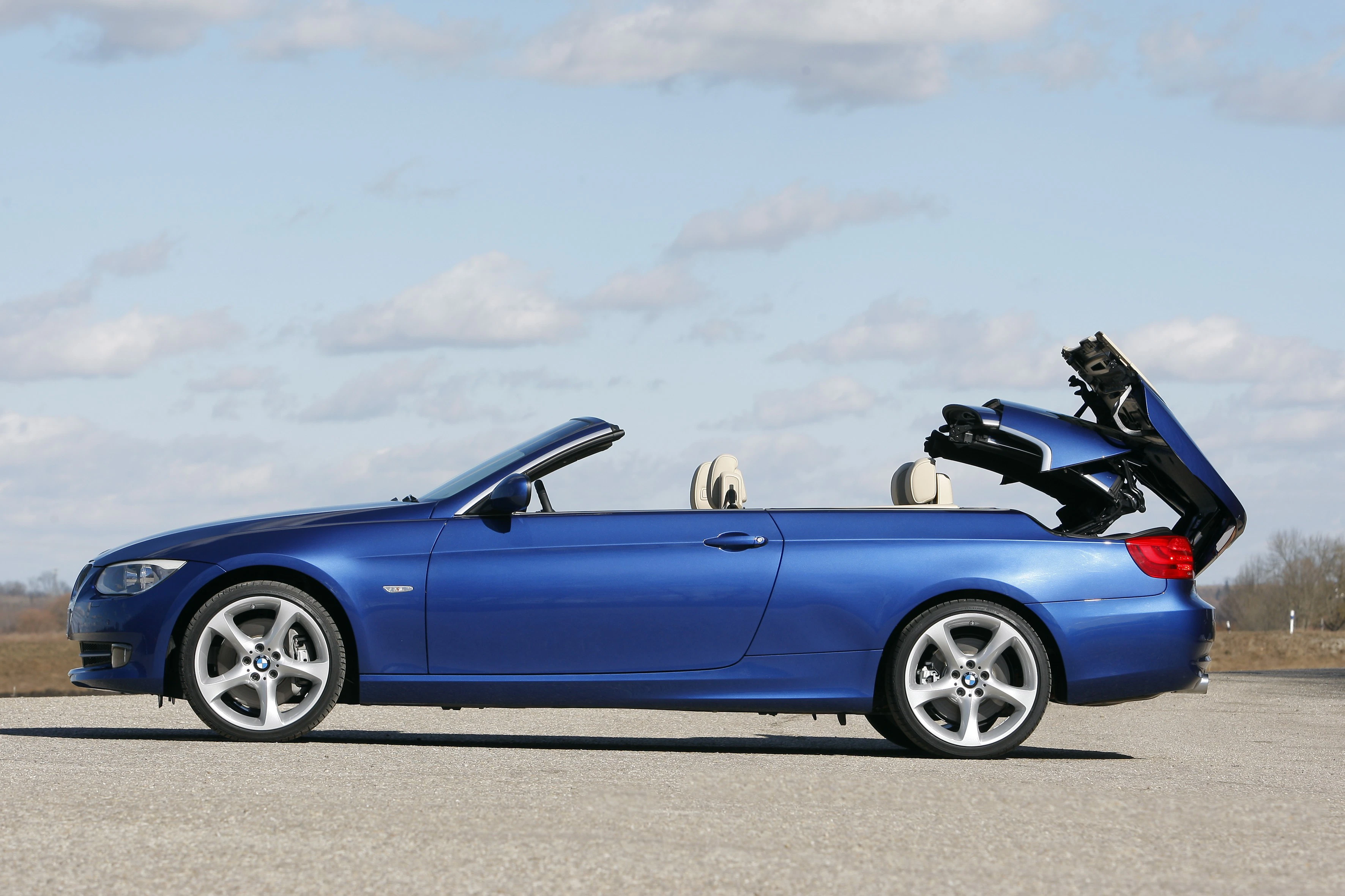 Blaues Cabriolet mit geöffnetem Verdeck auf einer Straße, im Hintergrund blauer Himmel und einige Wolken.