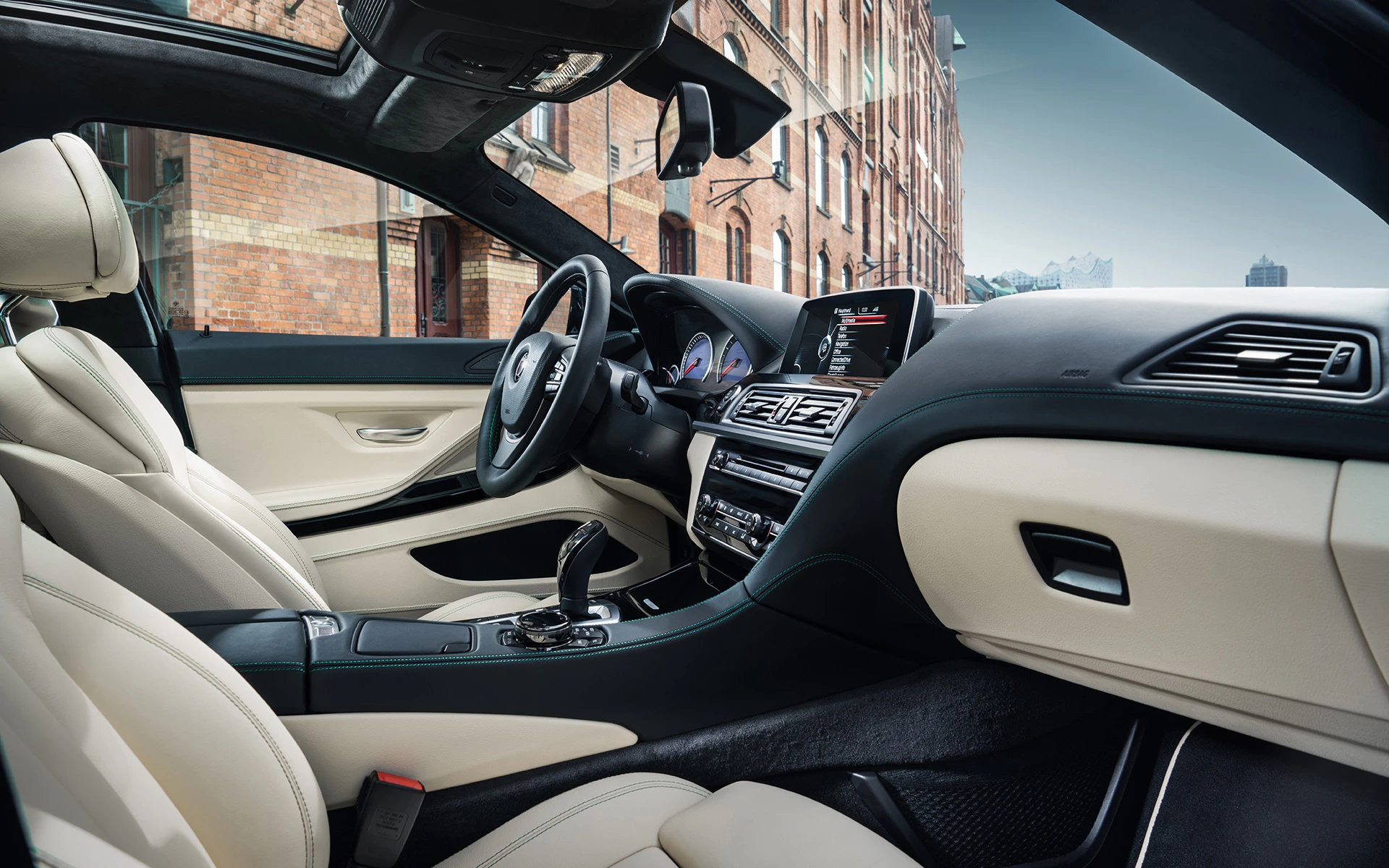 Innenraum eines modernen Autos mit beigen Ledersitzen, elegantem Armaturenbrett, Lenkrad und digitalem Display, im Hintergrund ein Backsteingebäude.
