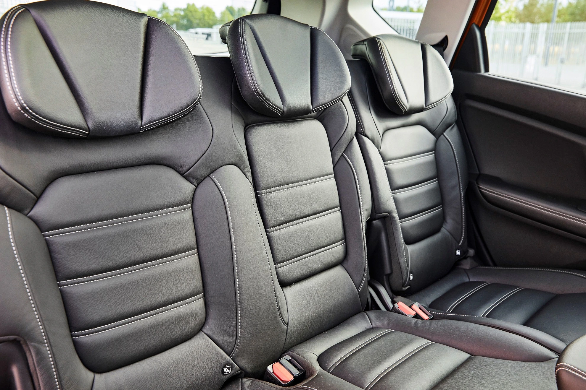 Schwarze Ledersitze im Auto zeigen drei bequeme Rücksitze mit Kopfstützen und Sicherheitsgurten in einer modernen Fahrzeugkabine.
