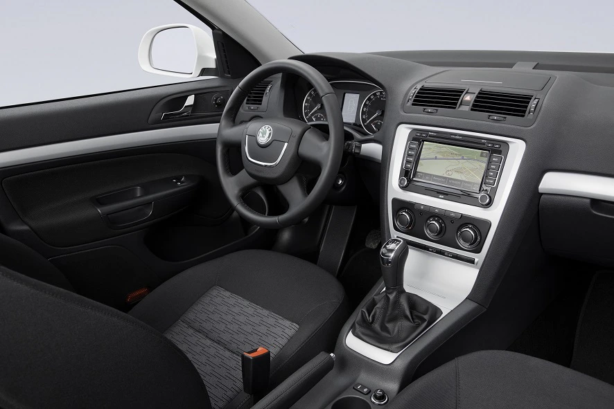 Innenansicht eines modernen Autos mit Lenkrad, Gangschaltung, Armaturenbrett und Navigationsbildschirm, bezogen in schwarzem Stoff.