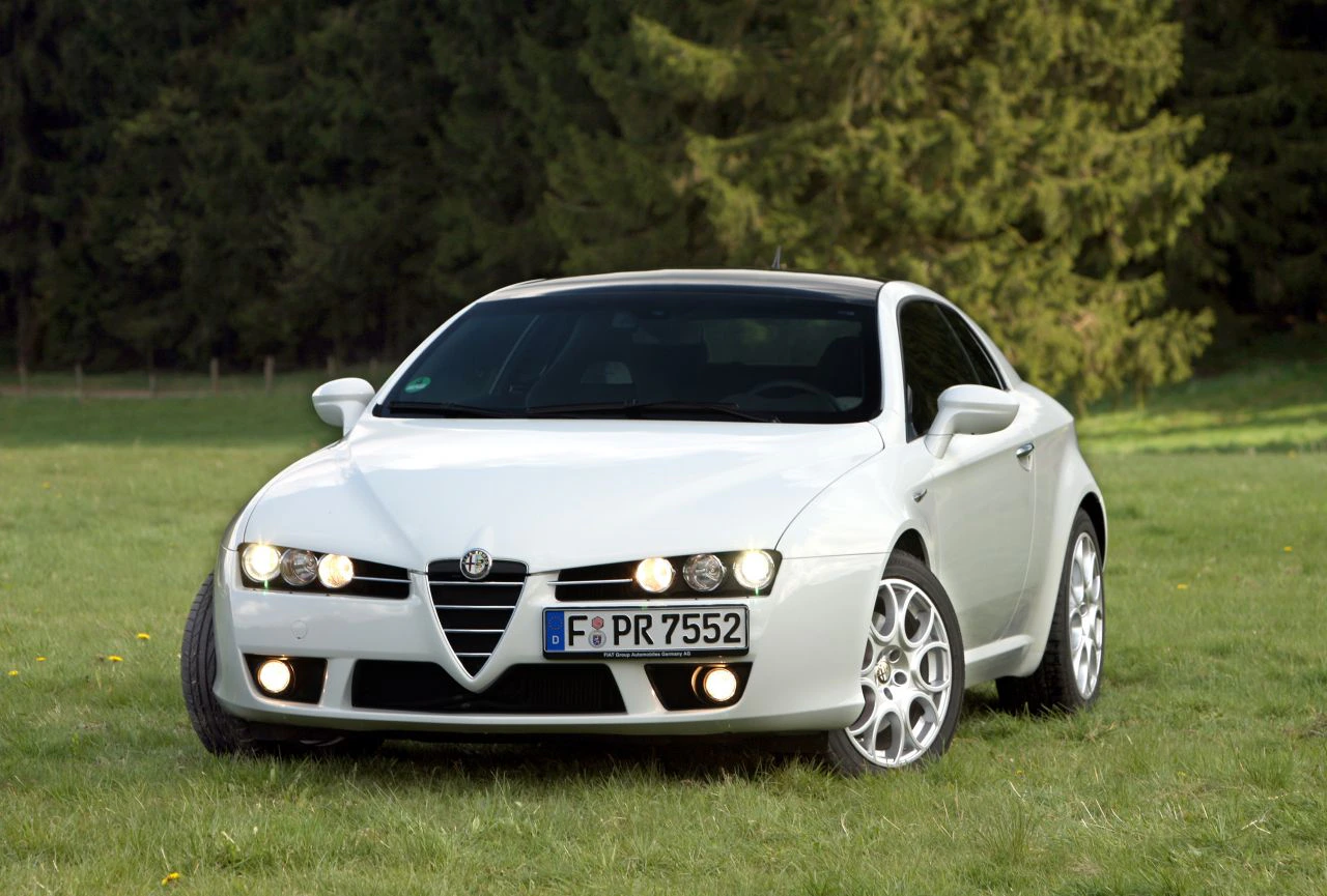 Weißer Alfa Romeo Brera auf einer grünen Wiese vor einem Hintergrund mit Bäumen.