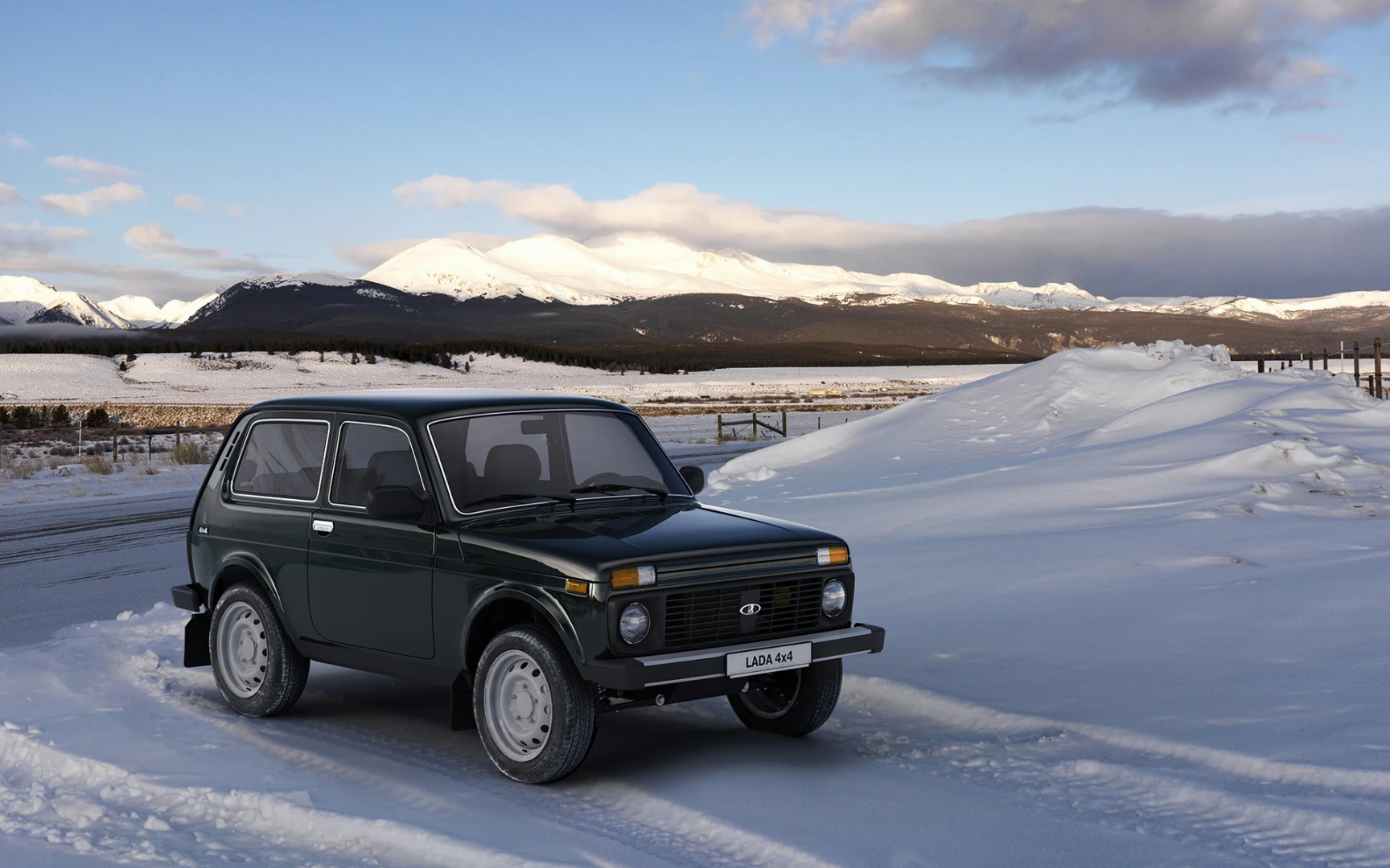 Ein grüner Geländewagen steht auf verschneitem Boden vor einer Bergkulisse mit bewölktem Himmel im Hintergrund.