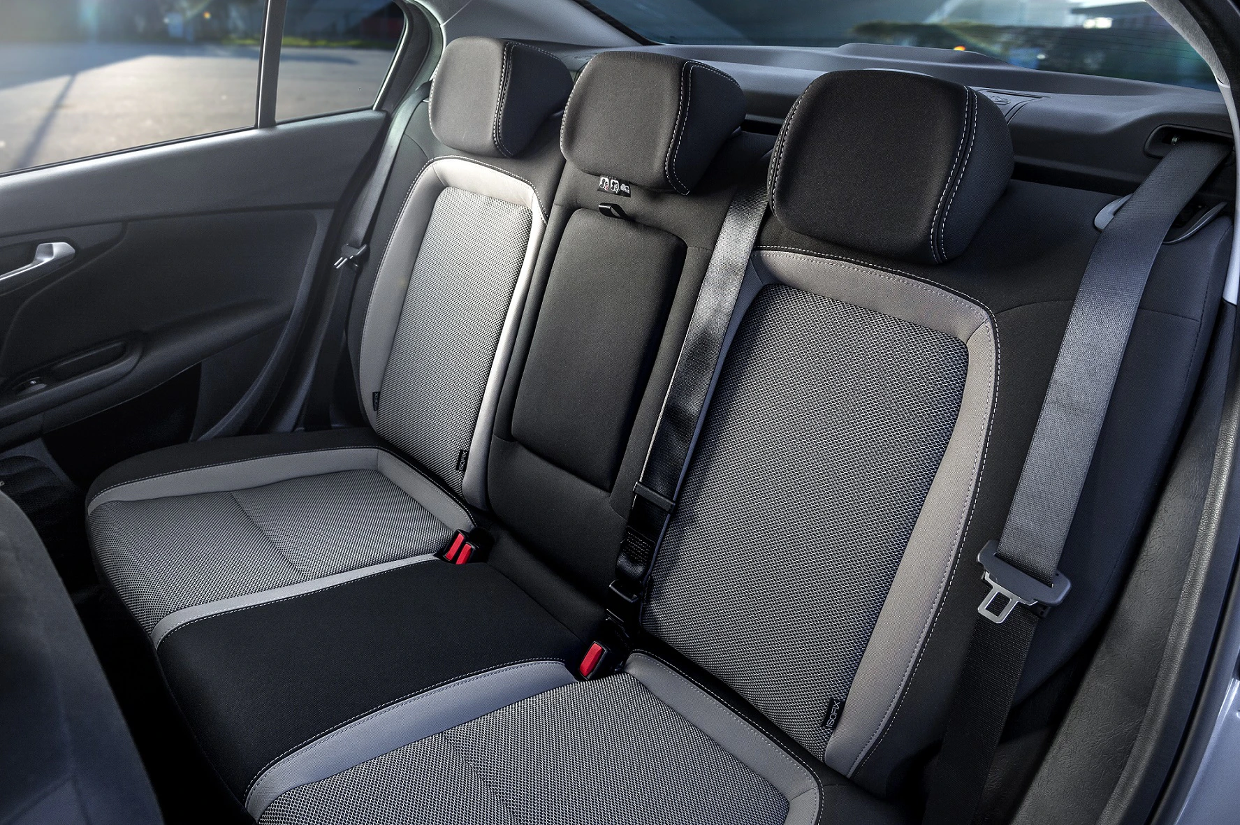 Rücksitz eines Autos mit drei schwarz-grauen Sitzen, Sicherheitsgurten und einem Fenster im Hintergrund.