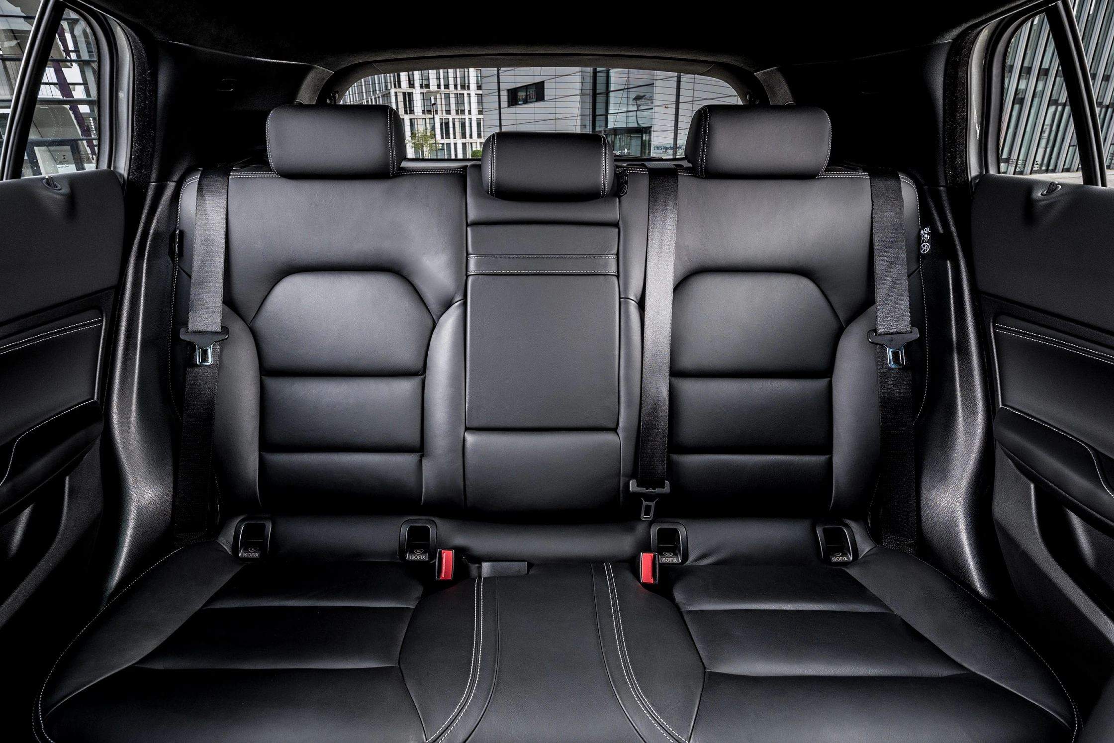 Schwarze Lederrückbank eines Autos mit drei Kopfstützen, Sicherheitsgurten und eleganter Innenausstattung.