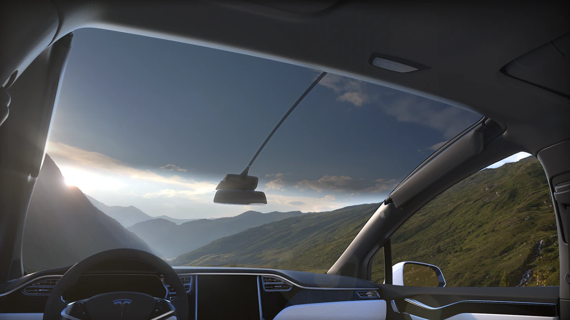 Innenansicht eines modernen Autos, das durch bergige Landschaft mit grün bewachsenen Hügeln und wolkenverhangenem Himmel fährt.