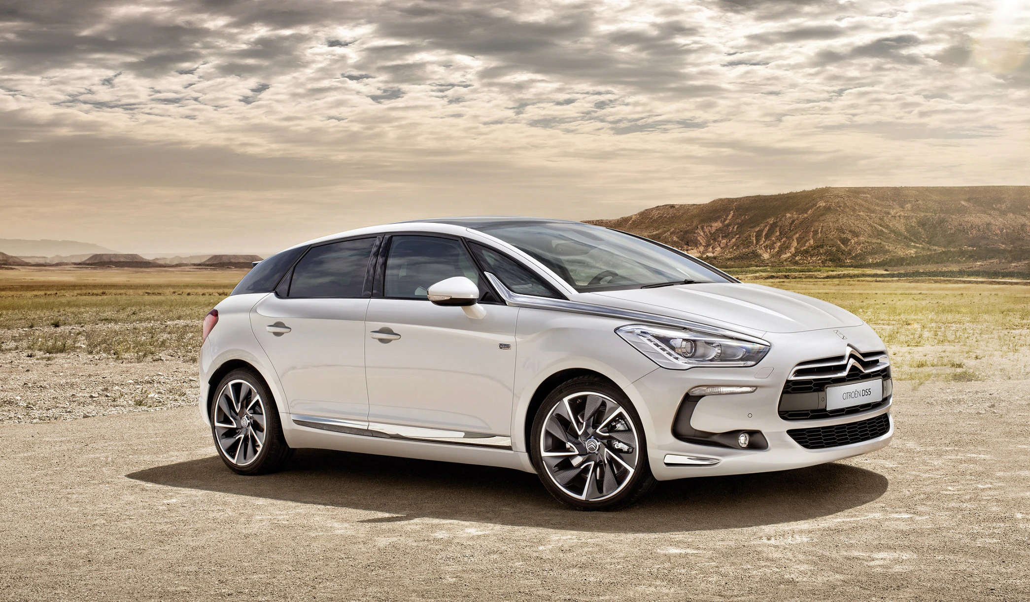 Weißer Citroën DS5 steht auf einer verlassenen Straße in einer kargen Landschaft unter bewölktem Himmel.
