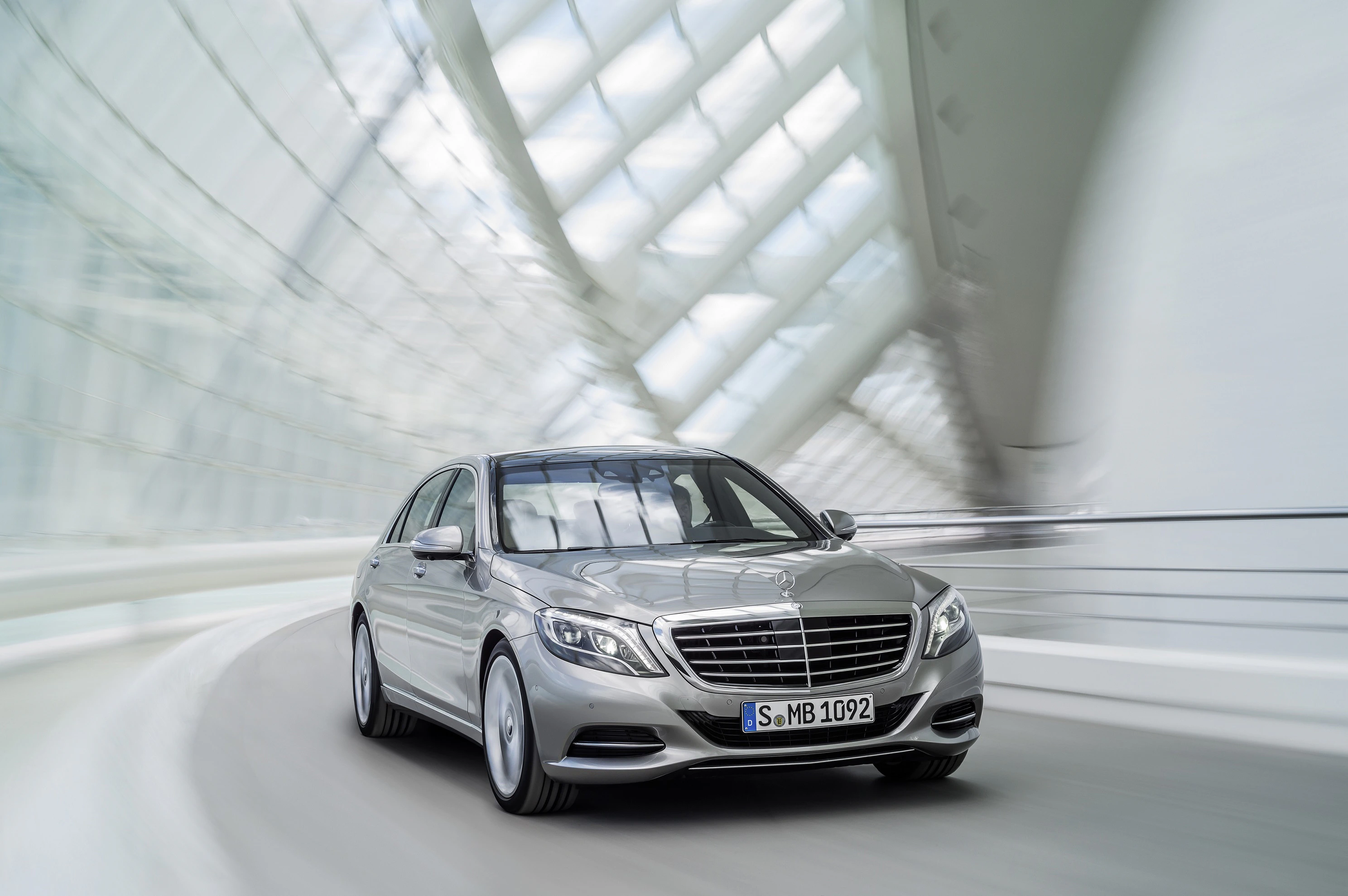Silberner Mercedes-Benz fährt dynamisch durch modernen, futuristischen Tunnel aus Glas und Stahl.