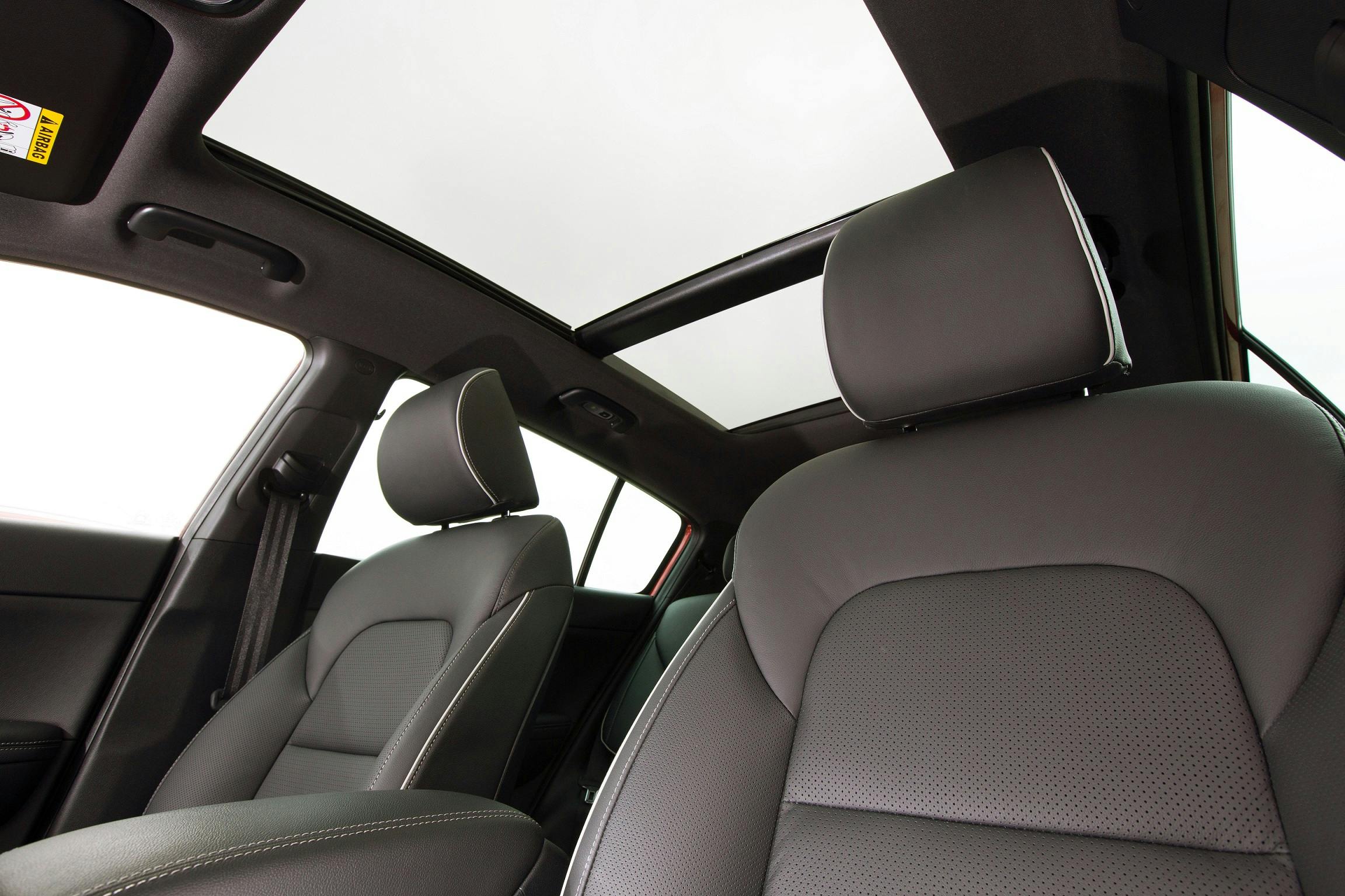 Innenraum eines Autos mit grauen Ledersitzen und geöffnetem Schiebedach, das Tageslicht hereinlässt.