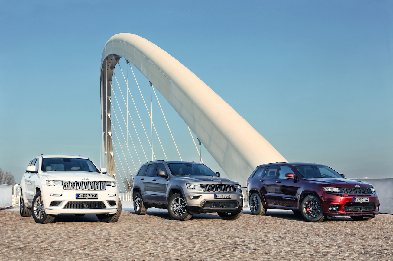 Drei parkende SUVs vor einer modernen, weißen Bogenbrücke unter klarem Himmel.