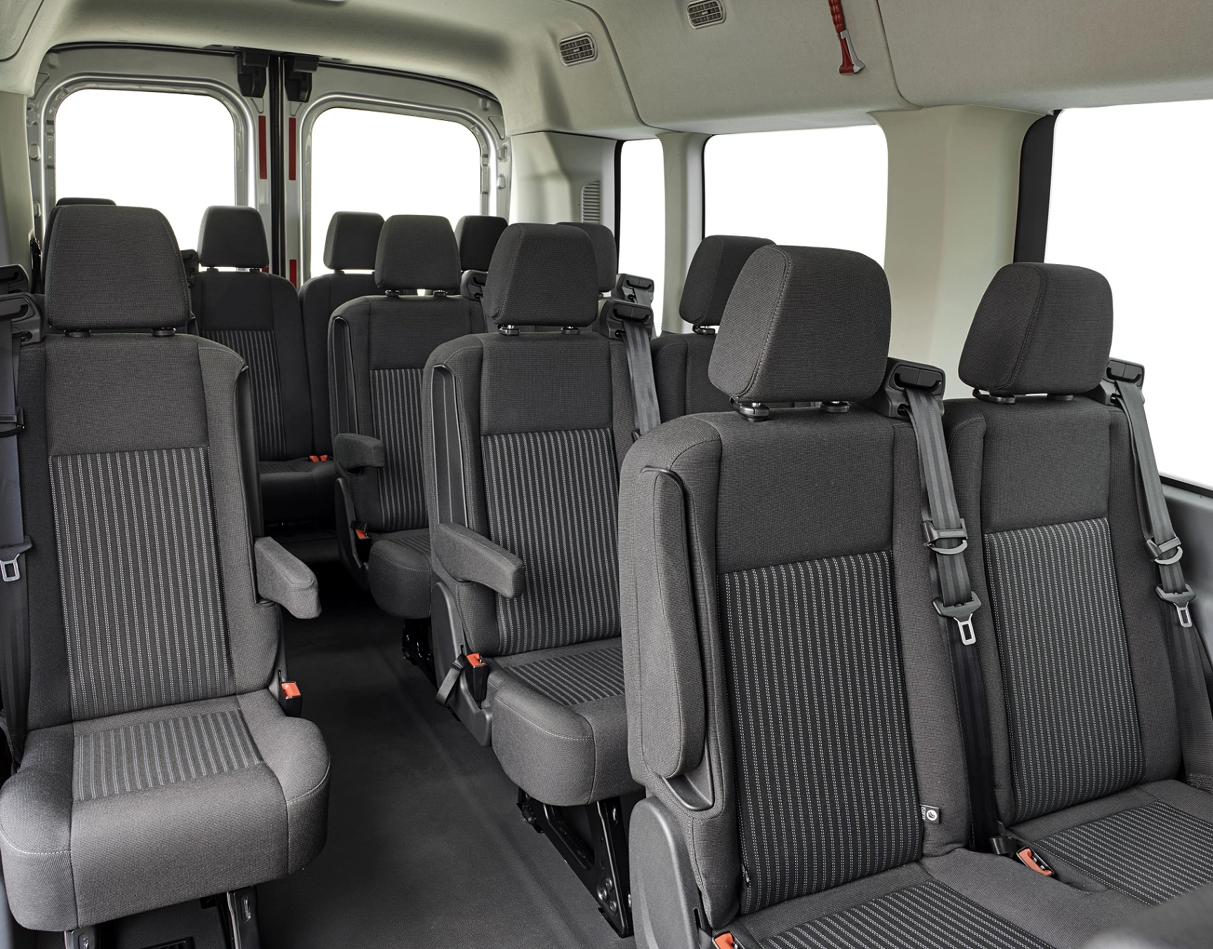 Innenraum eines leeren Transporters mit schwarzen Stoffpolstern, drei Sitzreihen und Sicherheitsgurten, in einer hellen Umgebung.