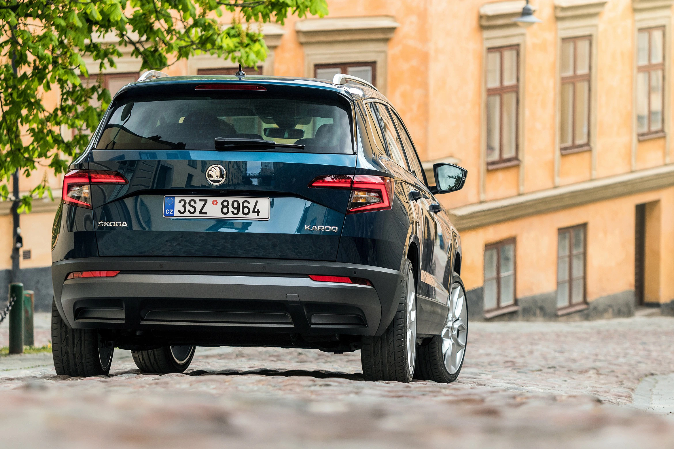 Ein blauer Skoda Karoq steht auf einem gepflasterten Weg, umgeben von historischen Gebäuden mit orangefarbenen Fassaden.