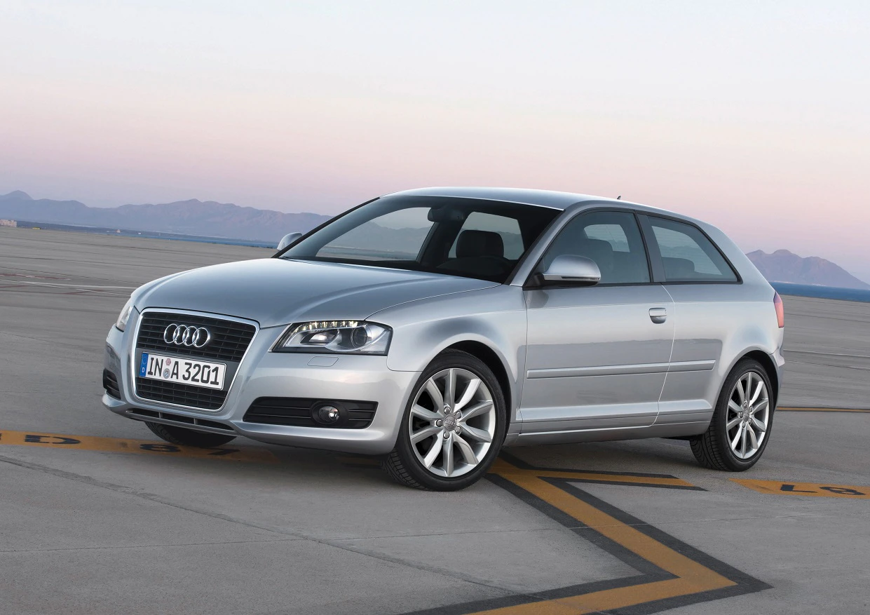 Silberner Audi A3 auf freier, asphaltierter Fläche bei Sonnenuntergang. Der Wagen ist schräg von vorne sichtbar.