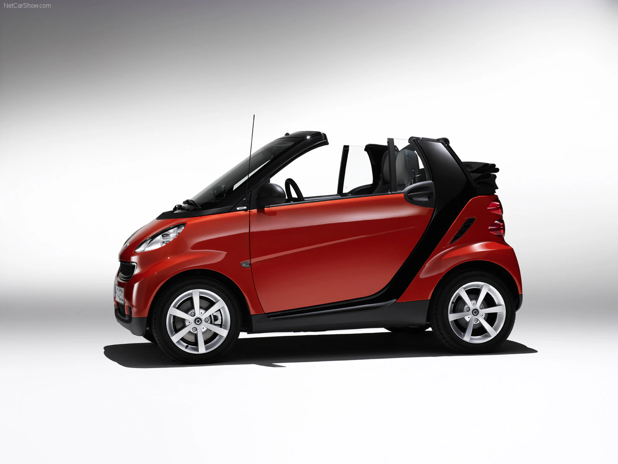 Roter Smart Cabrio mit schwarzem Dach, seitlich fotografiert vor weißem Hintergrund.