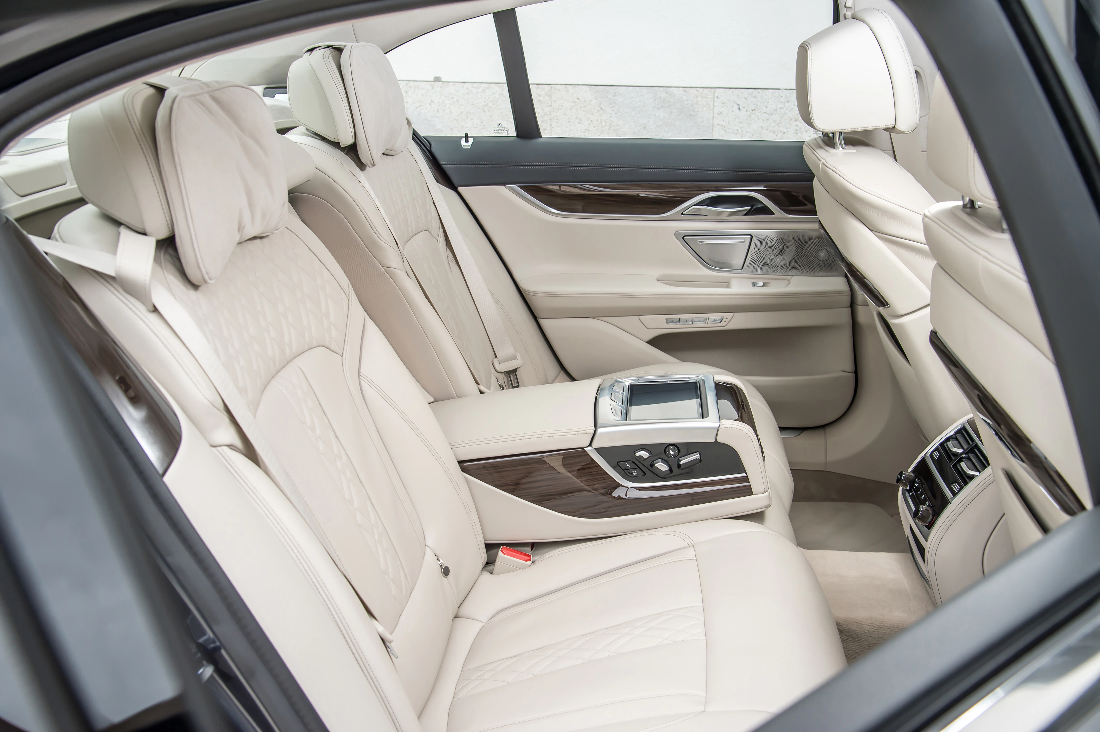 Hinteres Interieur eines Luxusautos mit beigen Ledersitzen, Holzakzenten und elektronischen Bedienelementen auf der Mittelkonsole.