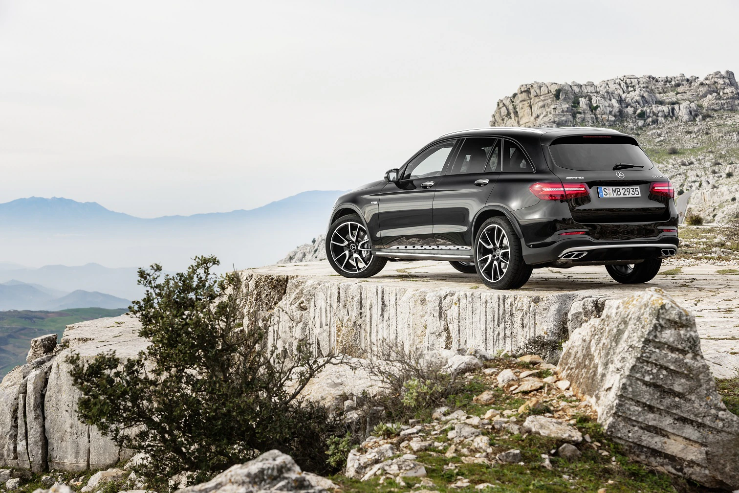 Schwarzes SUV parkt auf felsigem Aussichtspunkt mit Blick auf bergige Landschaft und bewölkten Himmel im Hintergrund.