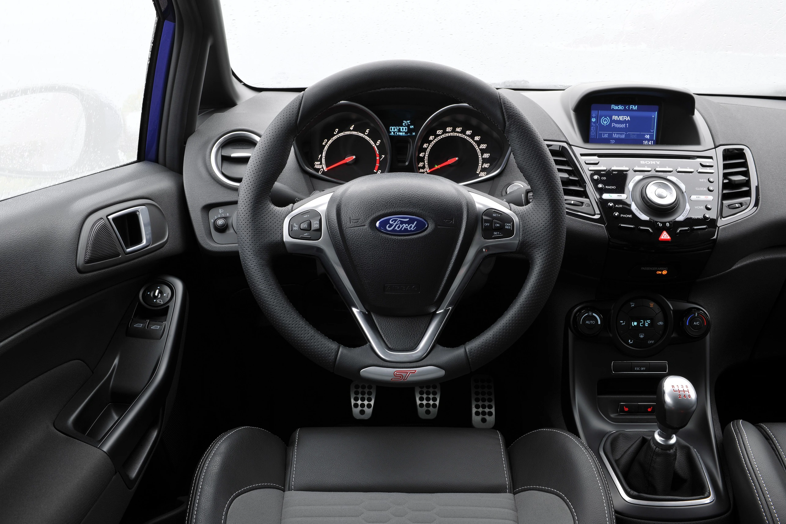 Blick auf das moderne Cockpit eines Autos mit Ford-Logo, zeigt das Lenkrad, Armaturenbrett mit Drehzahlmesser, Radio und manuelle Schaltung.