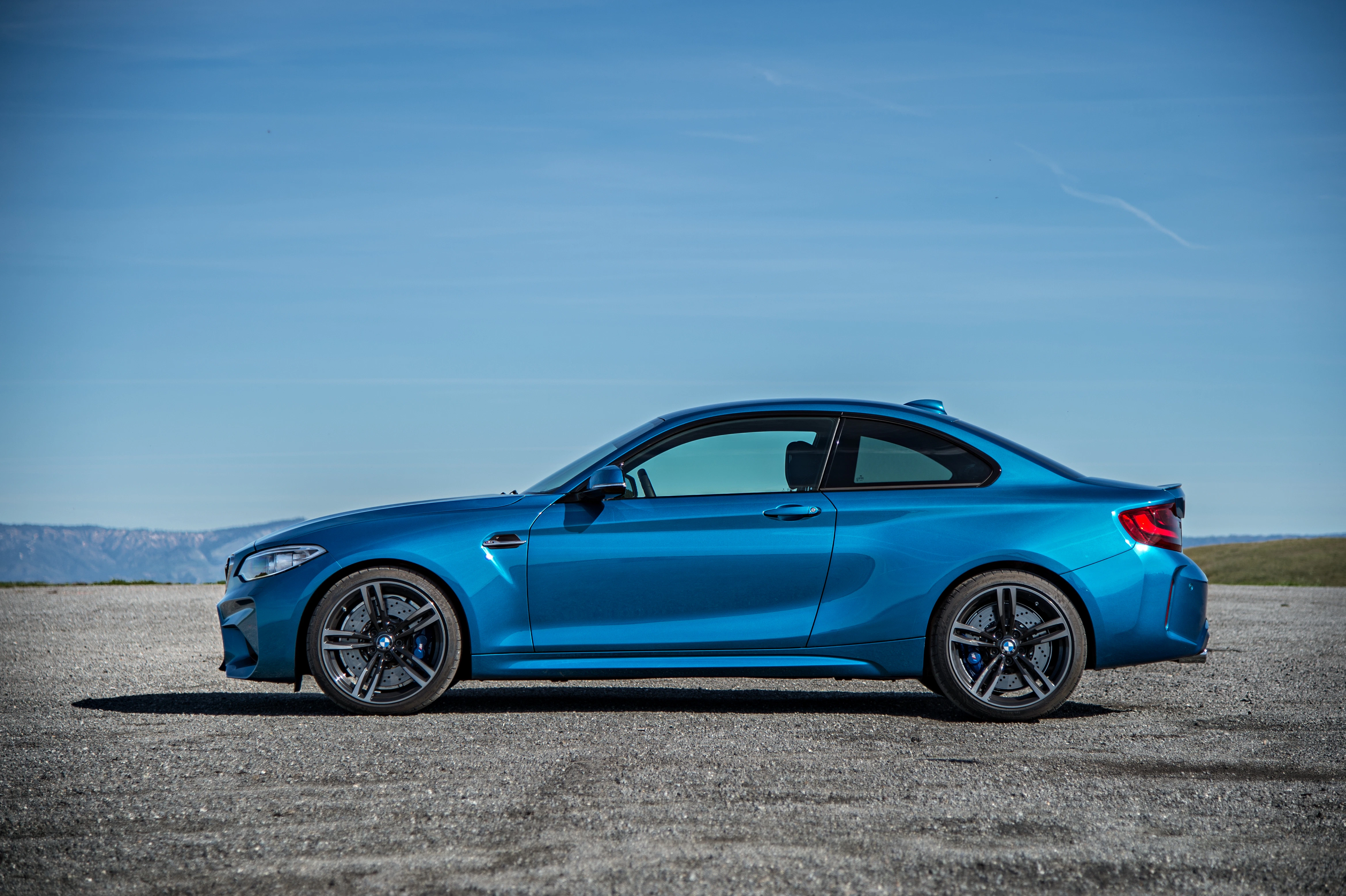 Blaues Sportcoupé auf freier, asphaltierter Fläche vor klarem Himmel. Auto von der Seite fotografiert, mittig platziert.