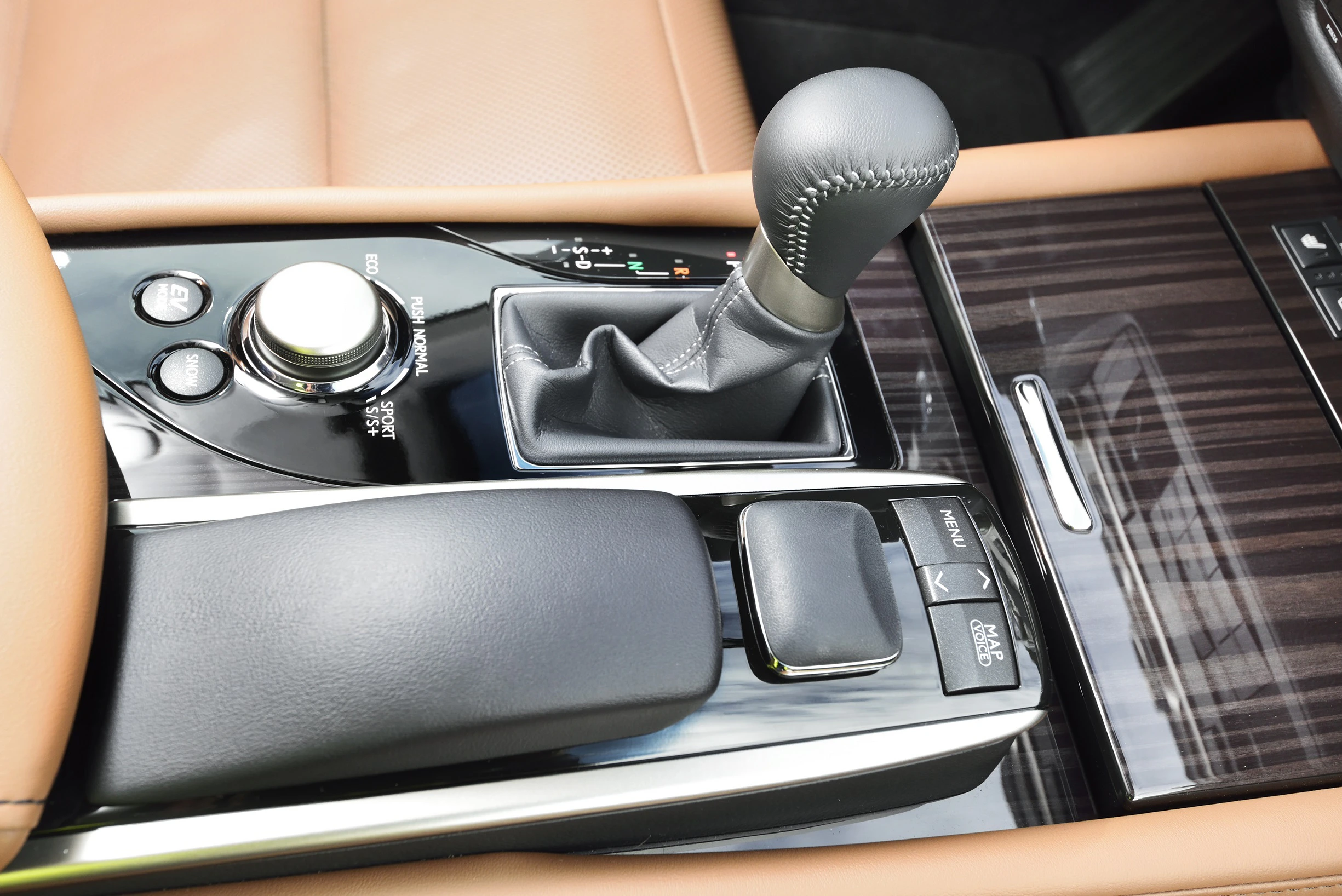 Nahaufnahme einer automatikgetriebenen Mittelkonsole mit braunem Leder, Holzverkleidung, Drehknopf und Schalthebel in einem modernen Auto.